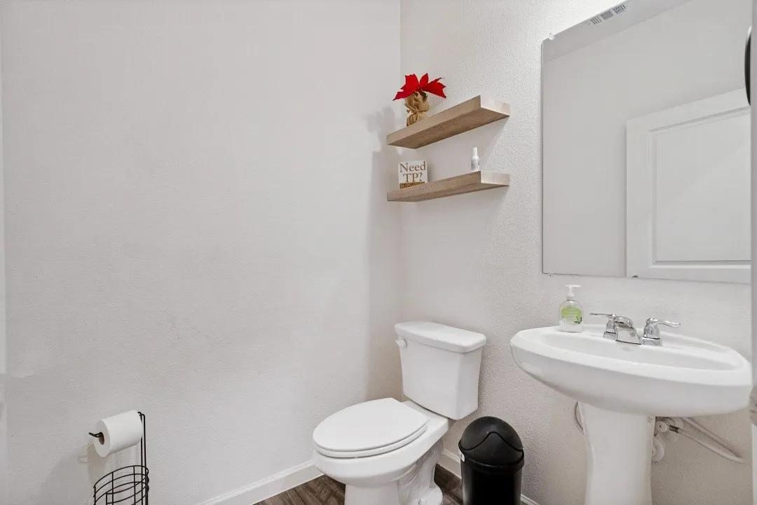 Pedestal sink with polished chrome fixtures, wood-finish floating shelves, and wood-finish flooring