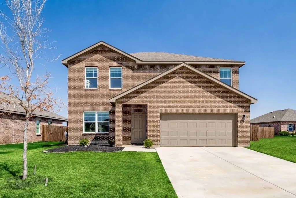 Two-story brick exterior with a two-car garage, concrete driveway, and established front landscaping