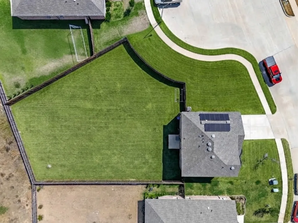 Expansive fenced backyard with a manicured lawn, paved driveway, and solar panel array on the roof