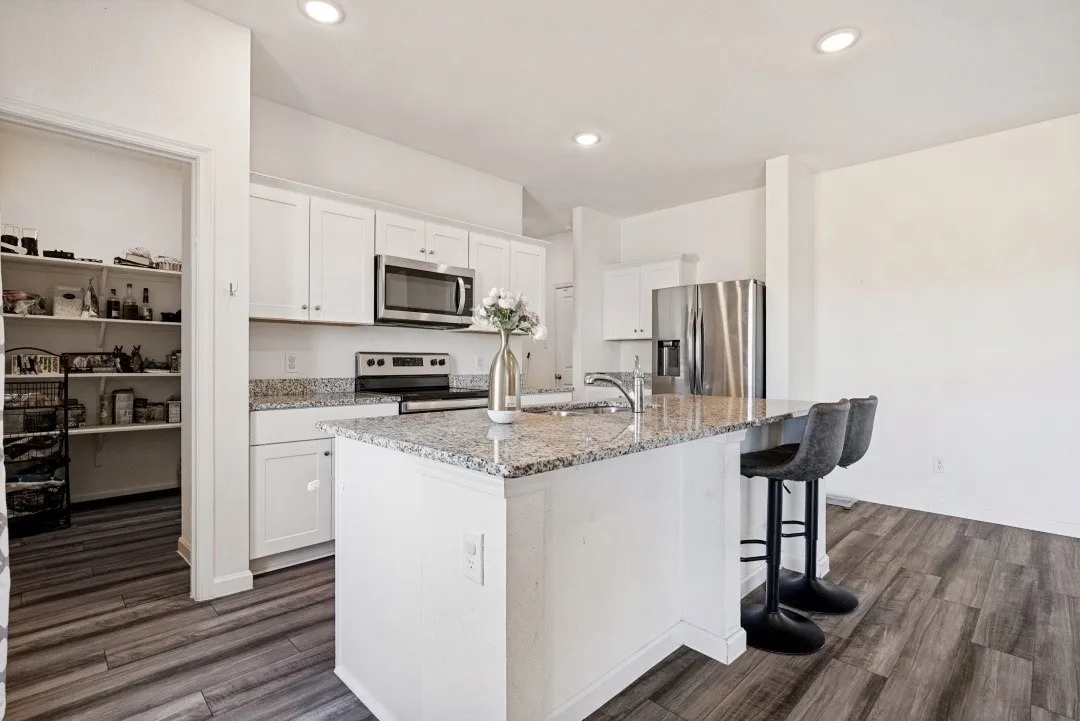 Kitchen featuring white cabinetry, stainless steel appliances, granite countertops, an island with seating, and wood-finish flooring