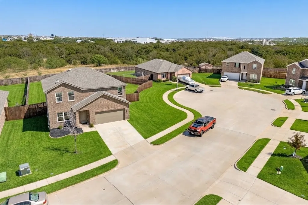 Red brick exterior with white trim, attached two-car garage, concrete driveway, and a front yard with manicured lawn
