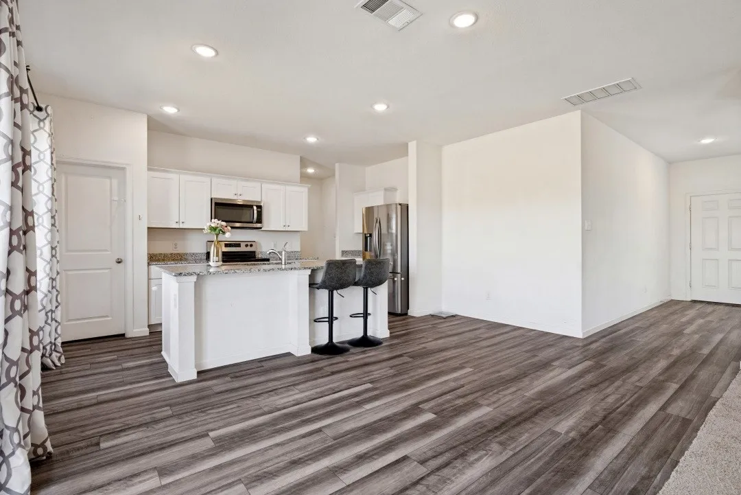 Wood-finish flooring throughout, kitchen island with seating, stainless steel appliances, white cabinetry, and recessed lighting