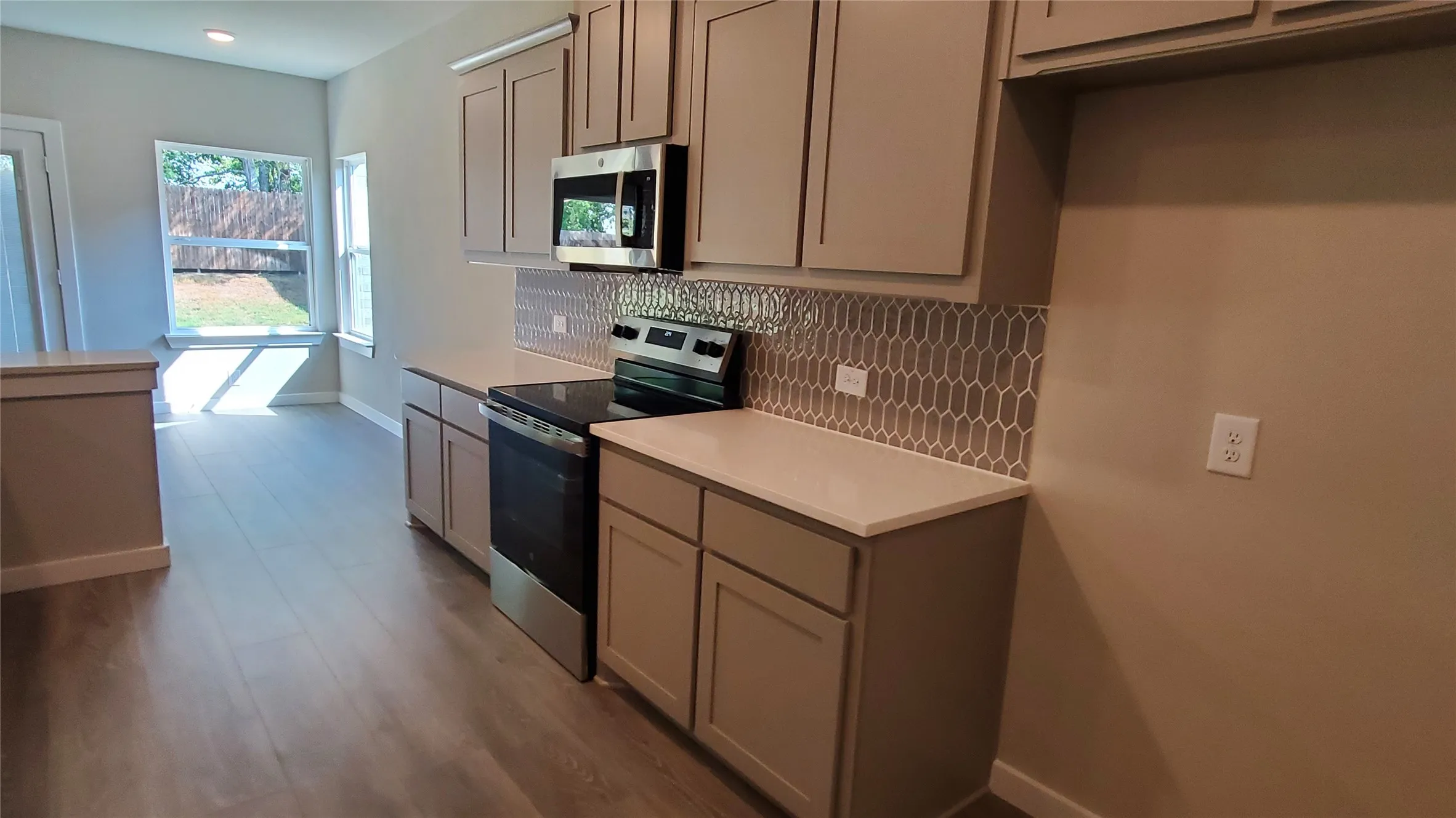 Kitchen featuring stainless steel appliances, light-toned cabinetry, solid surface countertops, and a mosaic tile backsplash