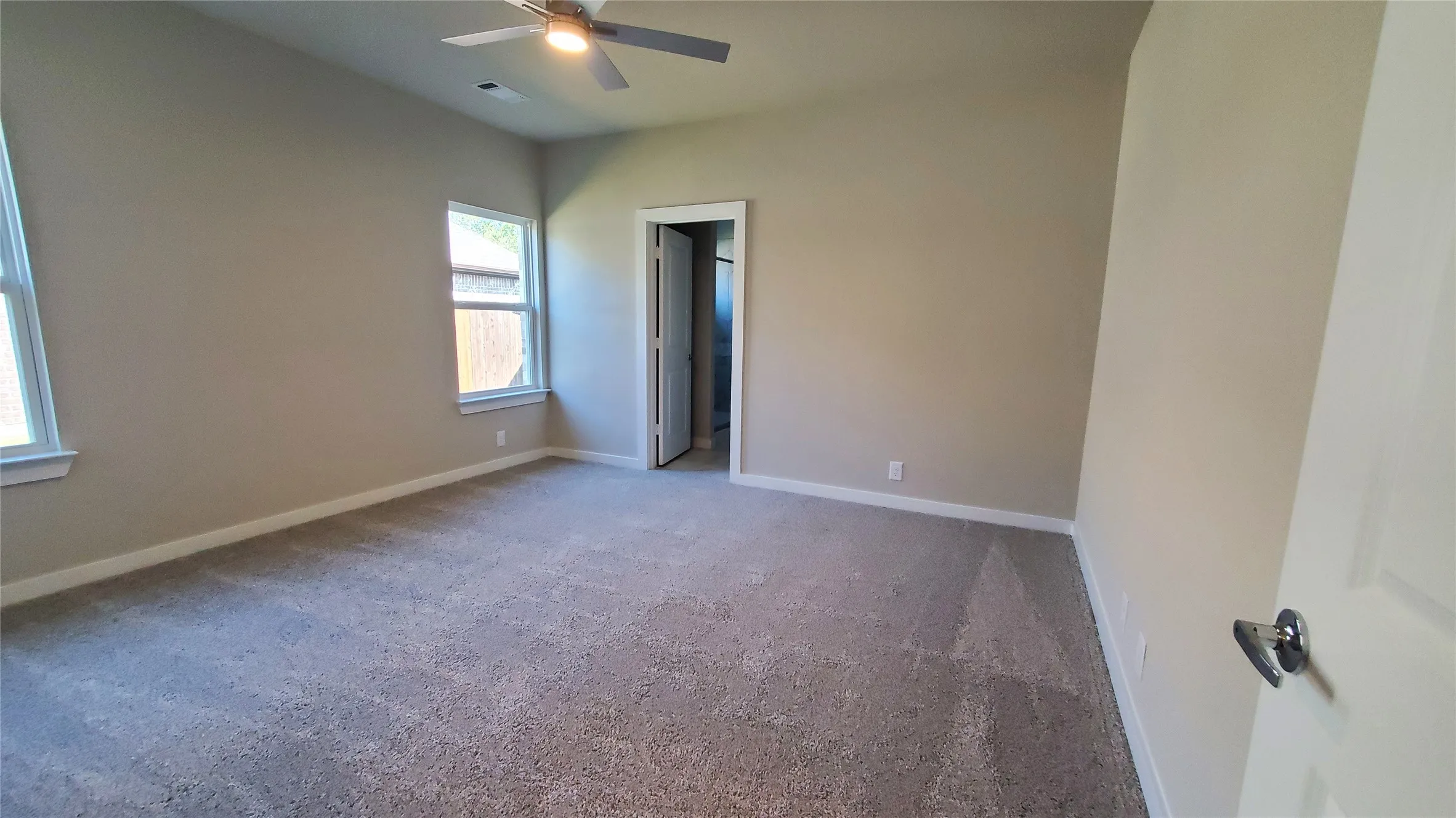 Vaulted ceiling with an attached ceiling fan, two windows, and neutral carpeting