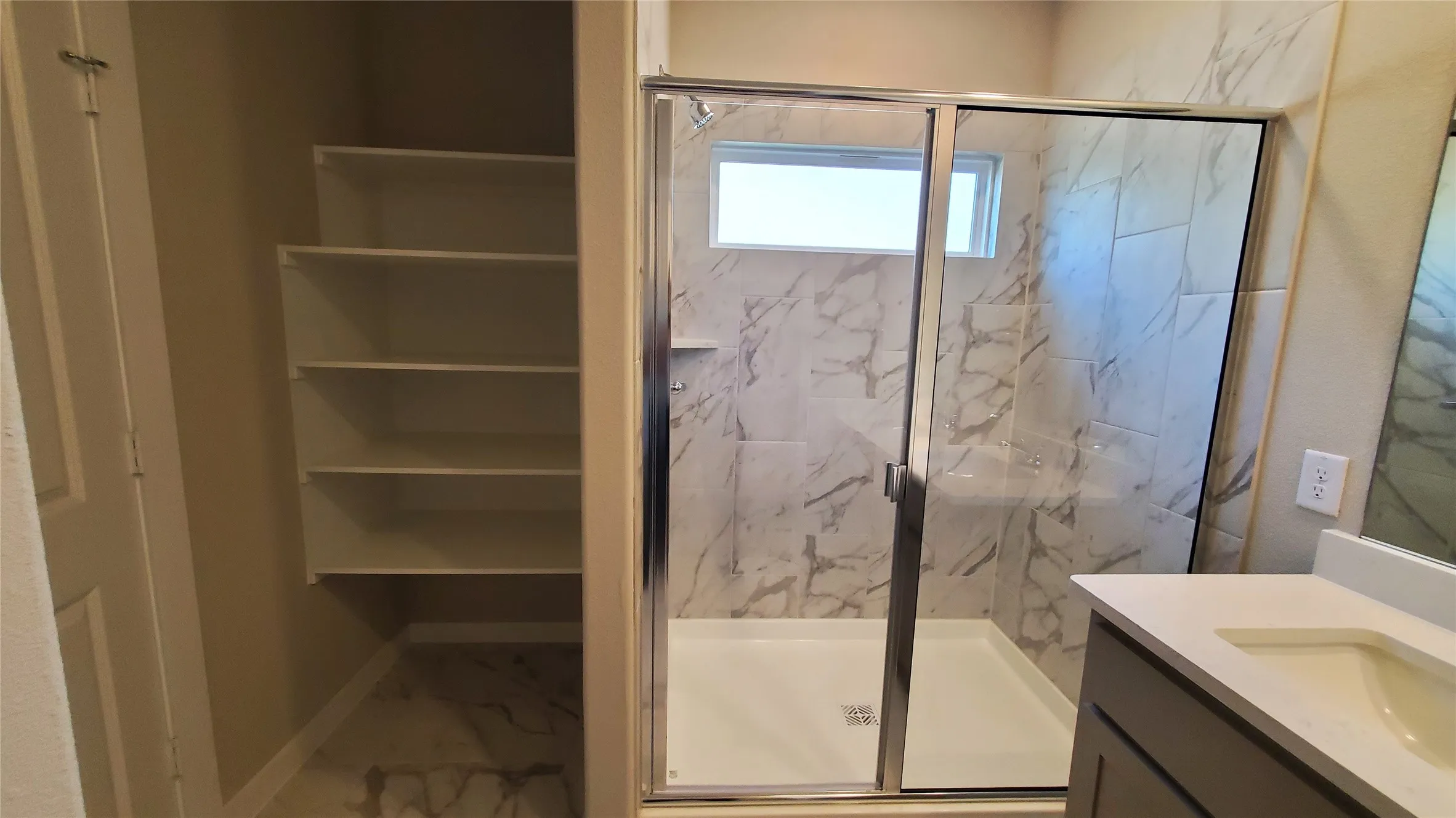 Built-in shelving, glass-enclosed shower with tile surround, integrated shower bench, fixed window, and single vanity with an undermount sink