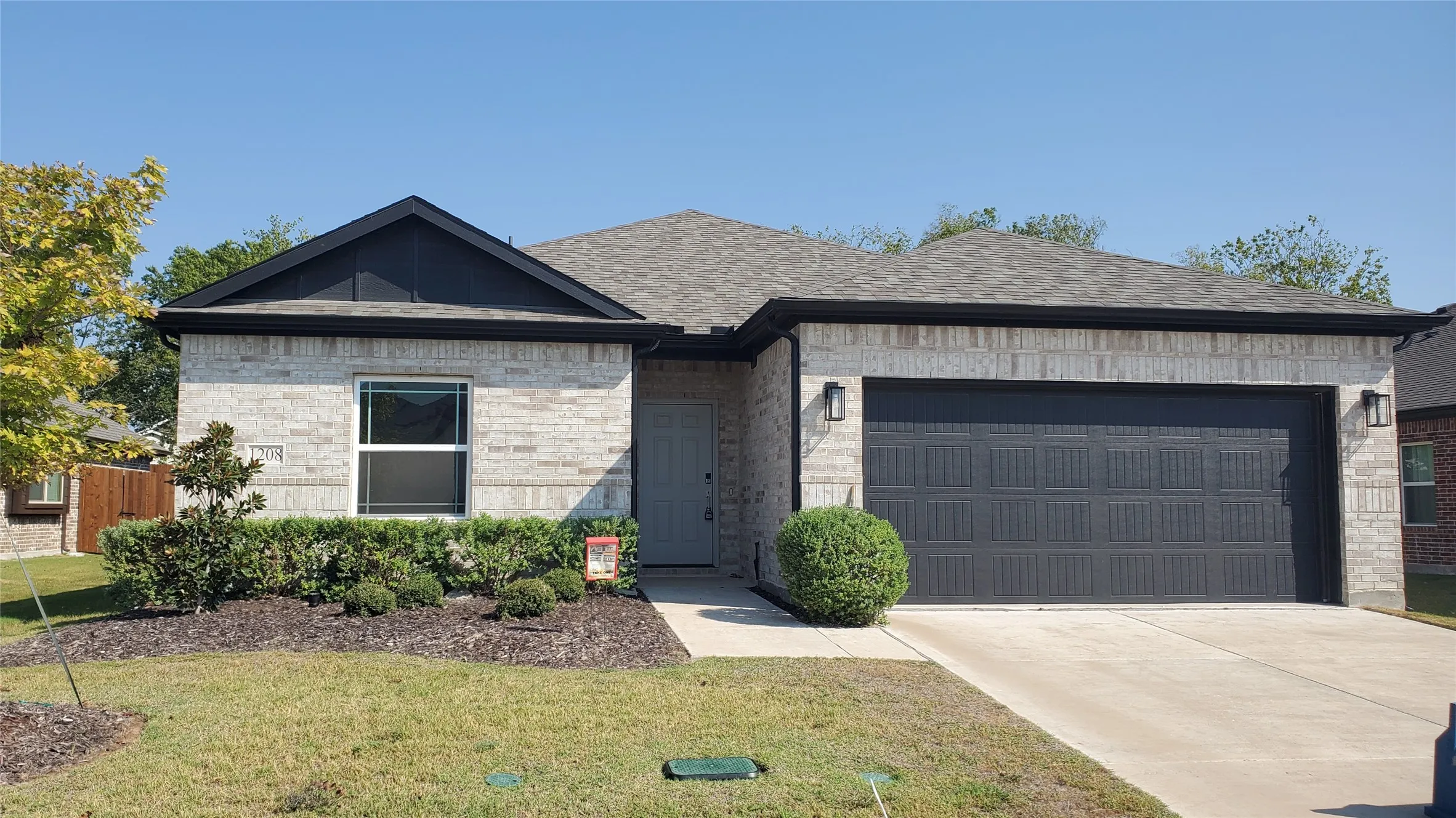 Light-colored brick exterior with a dark-toned garage door, featuring a gabled roofline and dark fascia