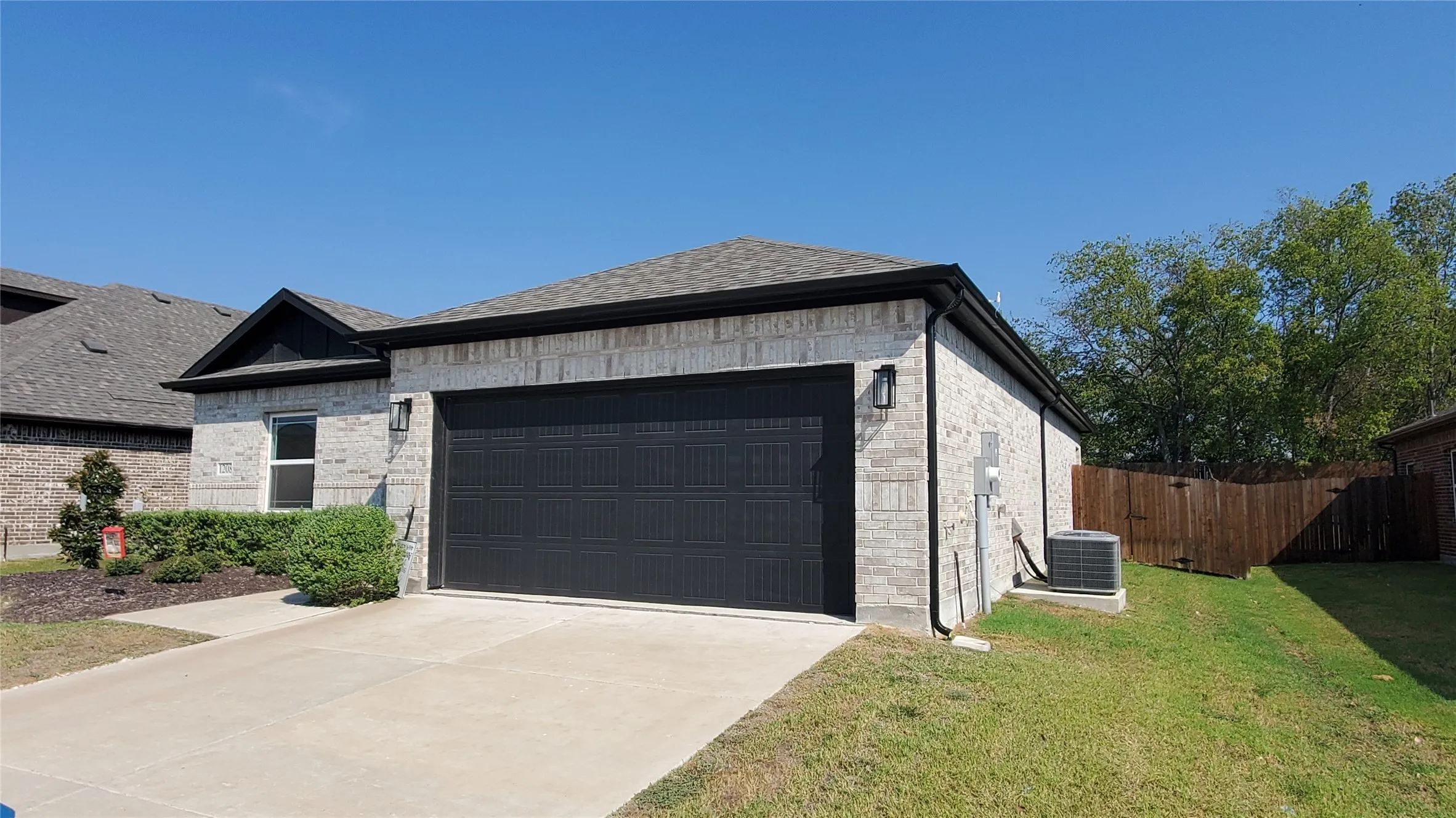 Light-colored brick exterior with dark trim, an attached garage, concrete driveway, and a wood privacy fence