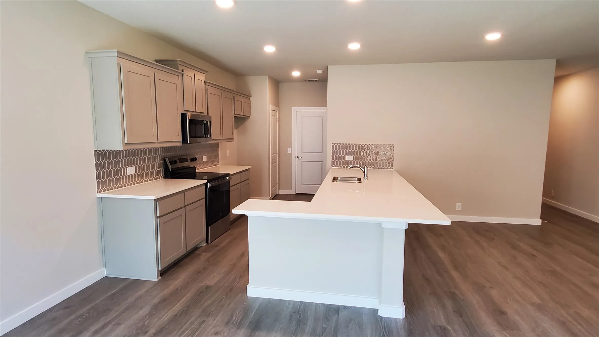 Kitchen featuring an island with a breakfast bar, stainless steel appliances, grey cabinetry, and a mosaic tile backsplash