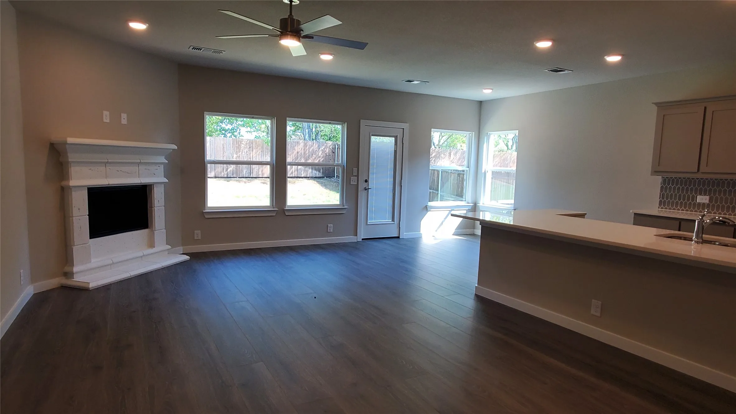 Spacious living area featuring wood-finish flooring, a decorative fireplace with a stone surround, and recessed lighting