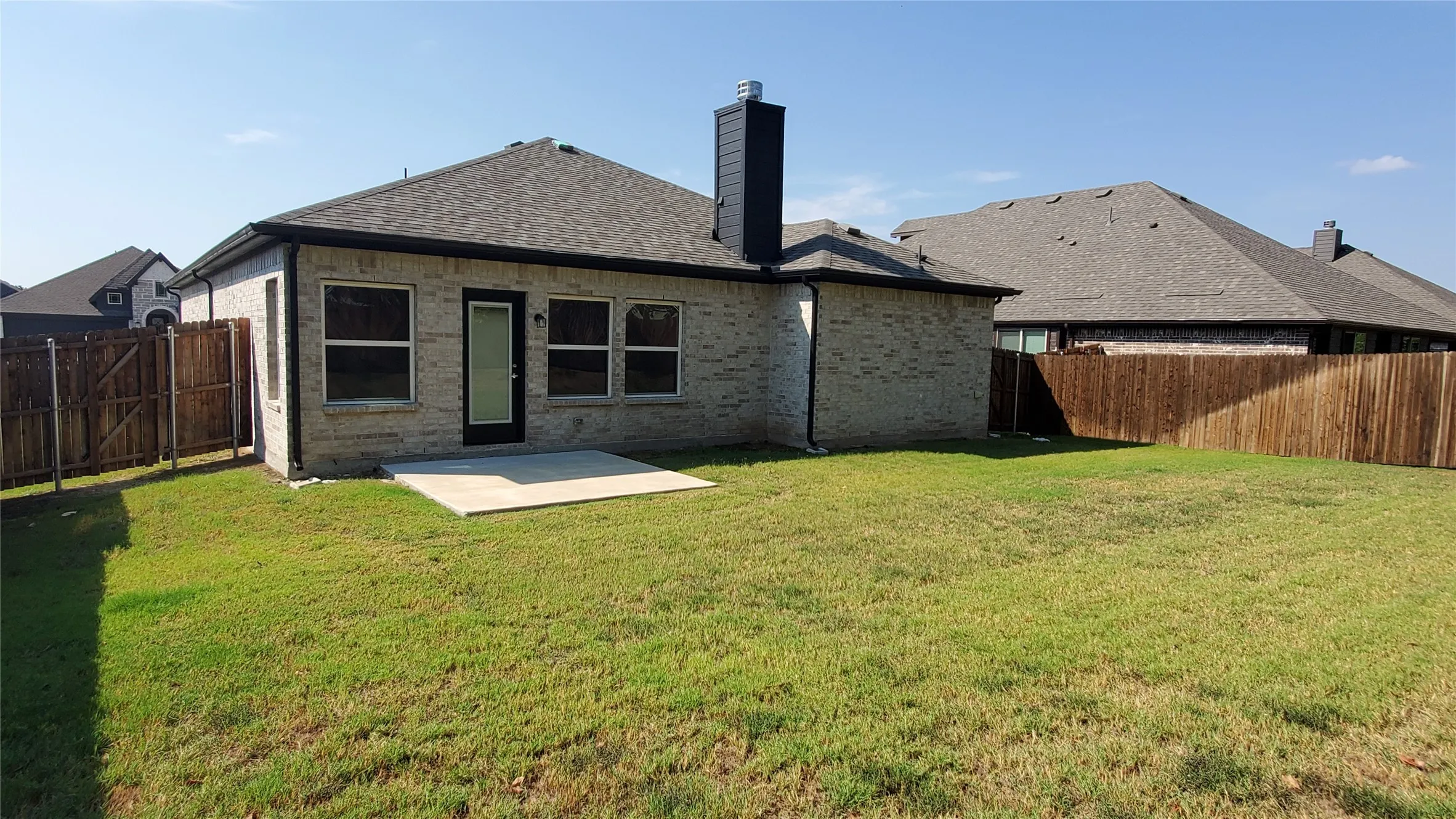 Brick exterior with a dark shingle roof, a concrete patio, and a wood privacy fence