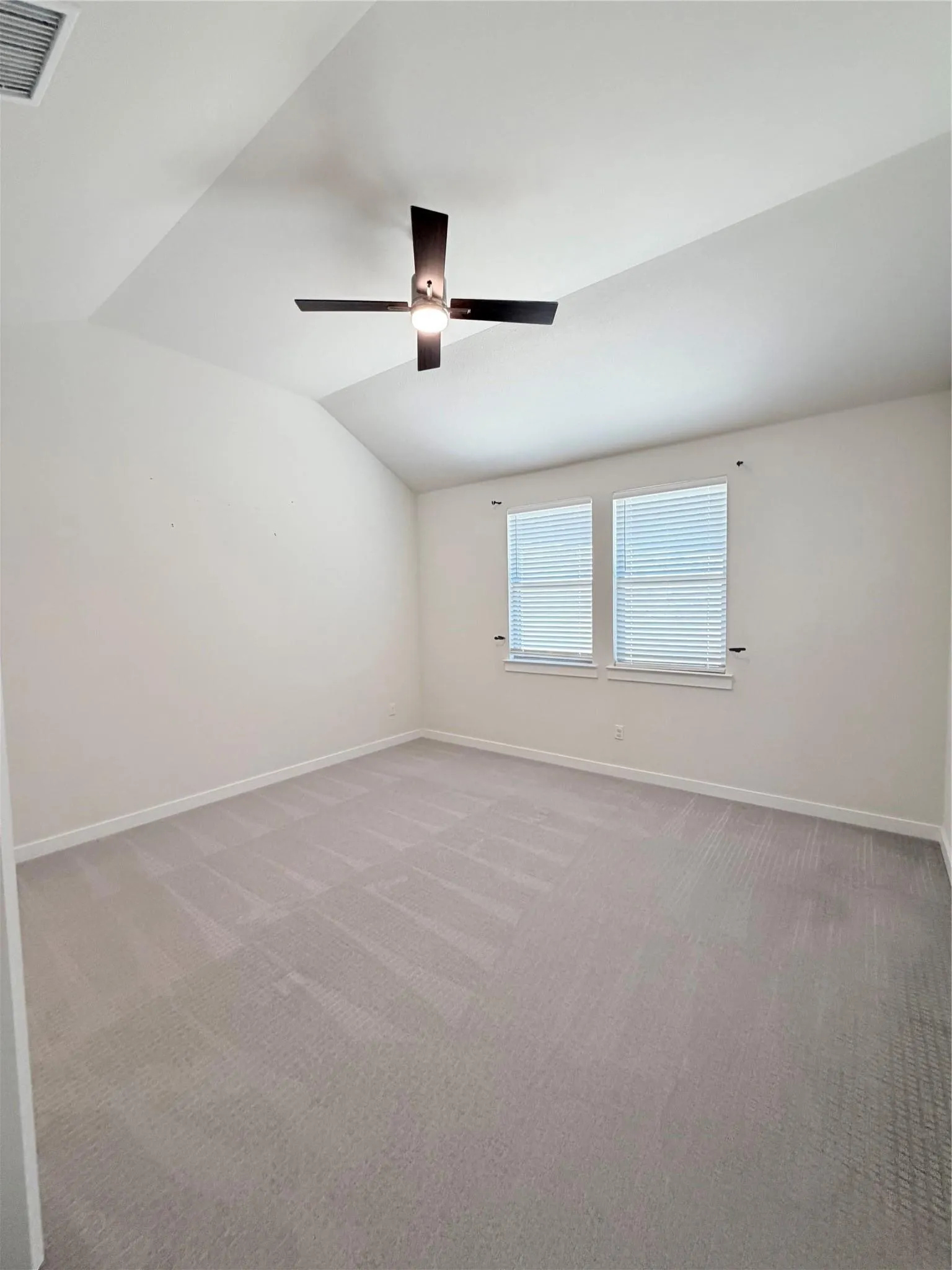 Vaulted ceiling, ceiling fan with integrated lighting, twin windows, blinds, and neutral tone carpeting