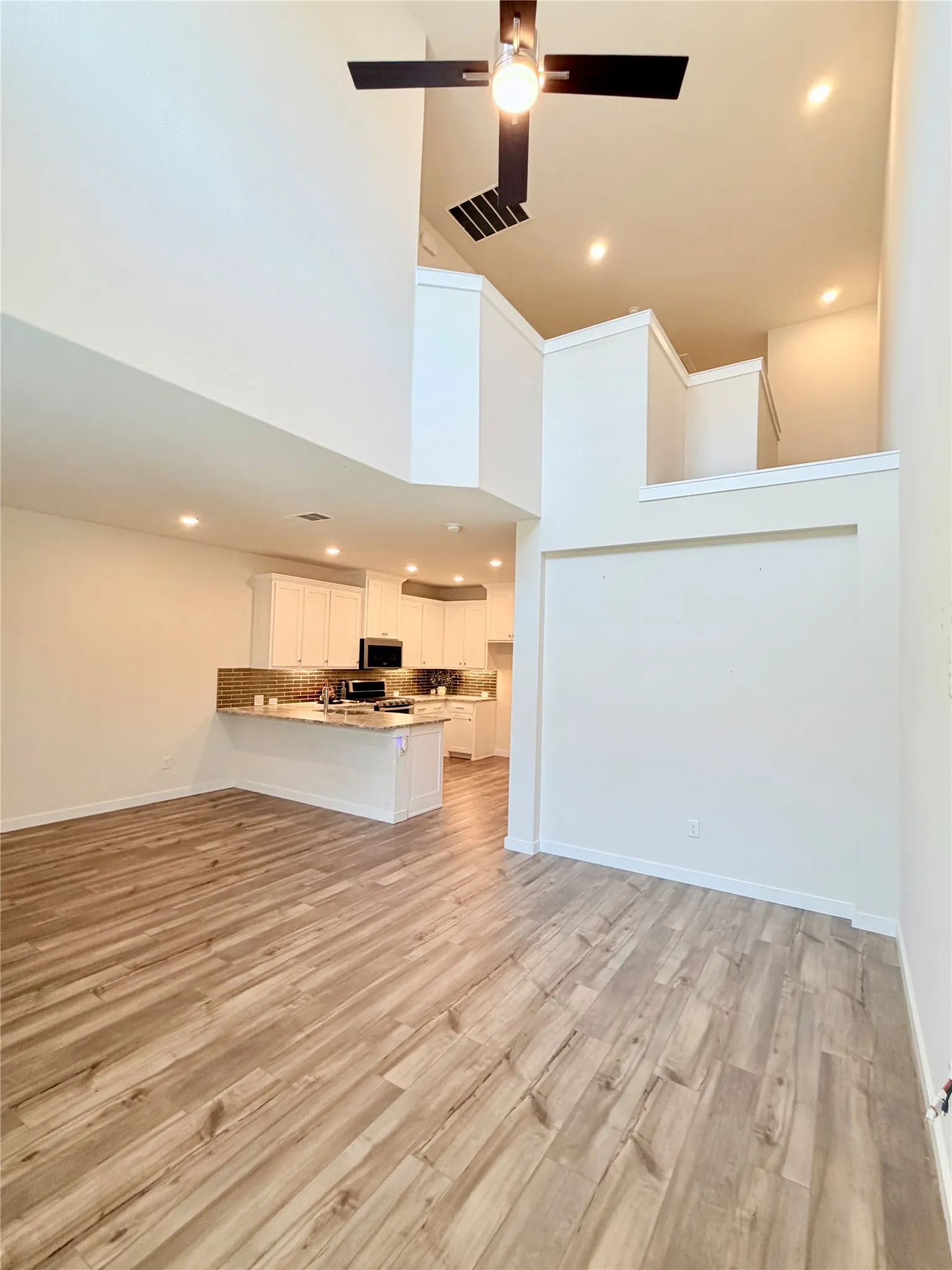 High ceilings with recessed lighting and a ceiling fan, wood-finish flooring, and a kitchen featuring a breakfast bar with stone countertop and tile backsplash