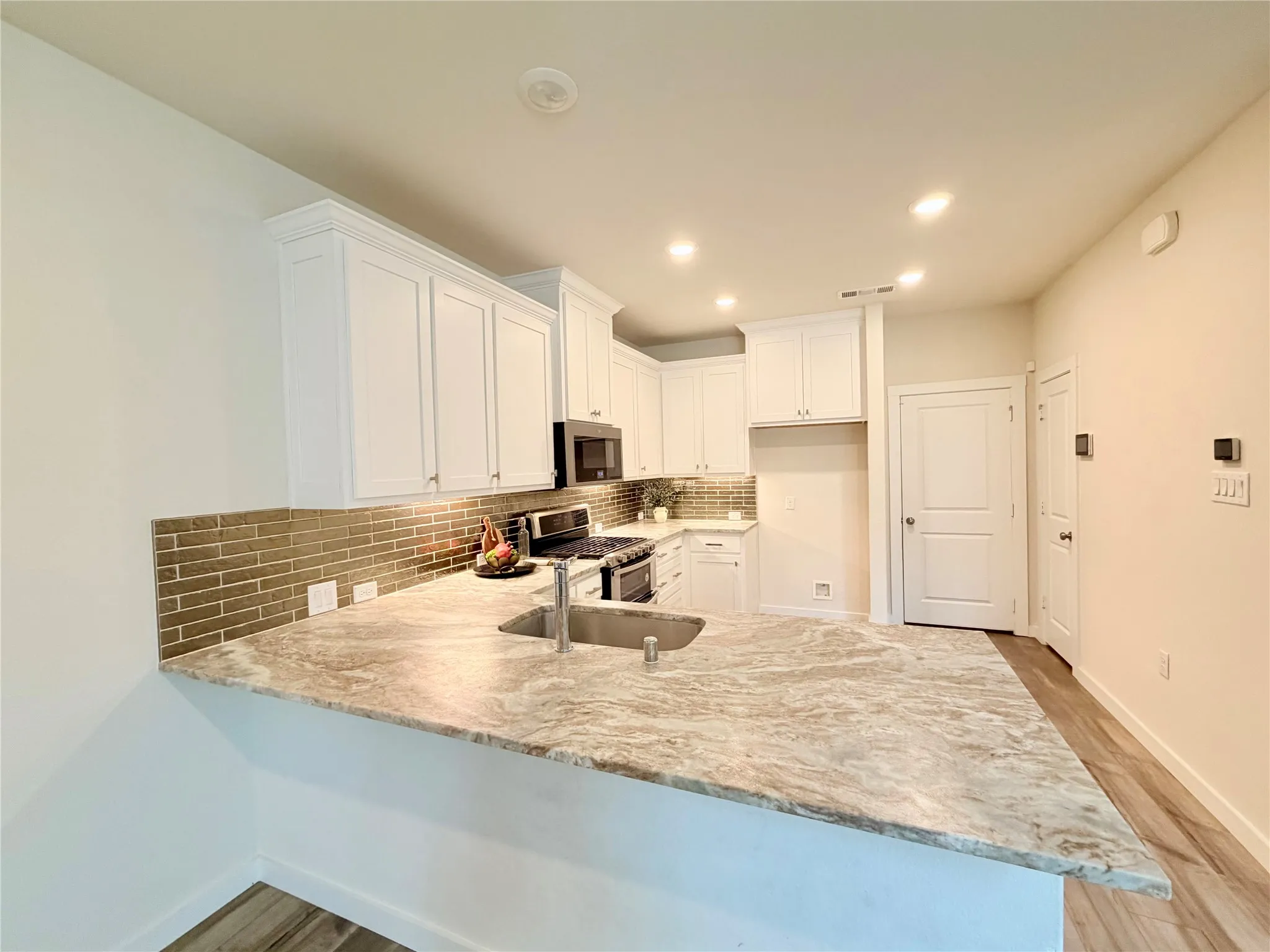 Kitchen featuring white cabinetry, a large kitchen island with an undermount sink, brick-patterned backsplash, and recessed lighting