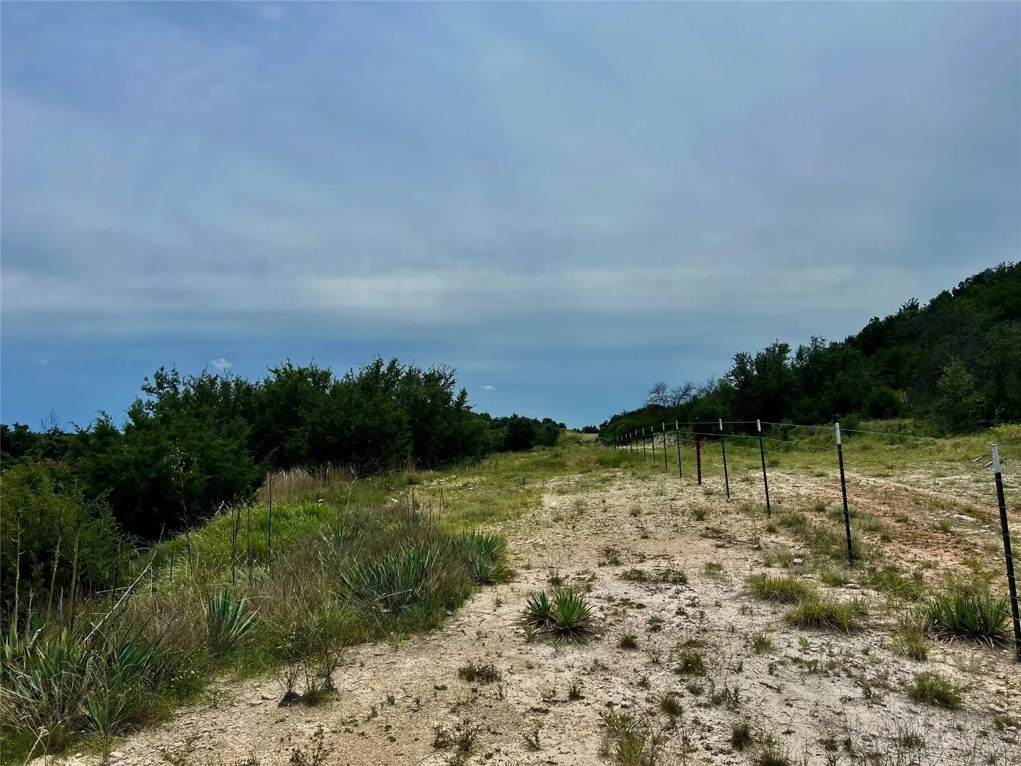 Expansive land featuring natural vegetation, partial fencing, and a clear sky backdrop