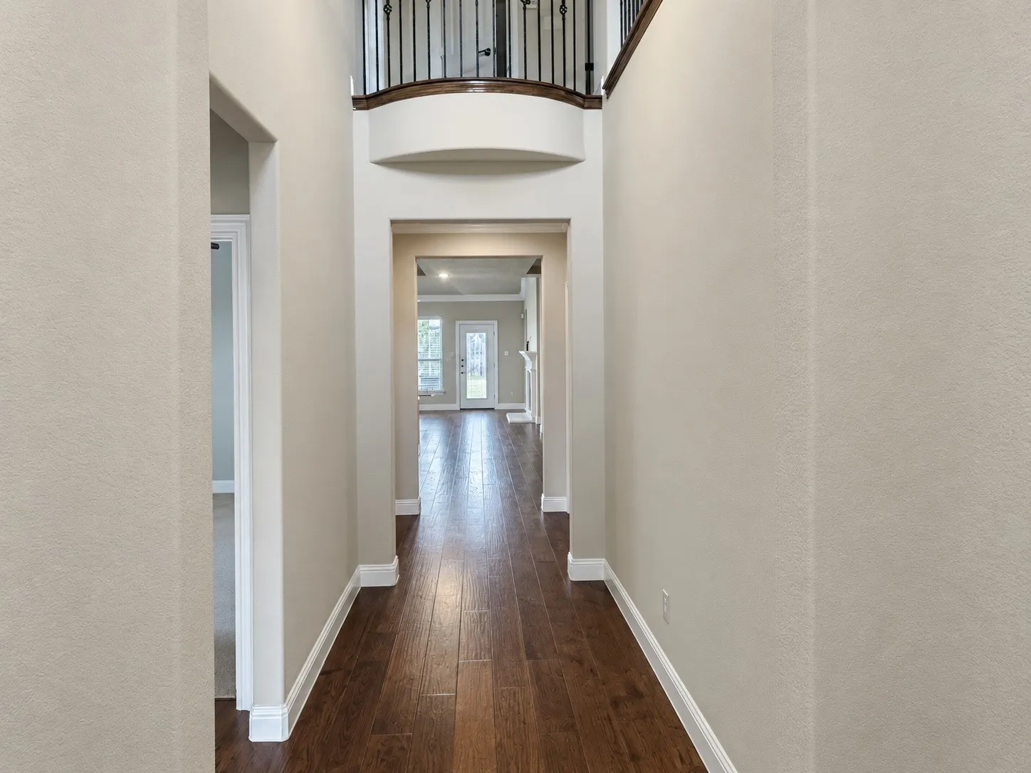 Entryway featuring wood-finish flooring, light-toned walls, and a prominent second-story balcony with wrought iron balusters