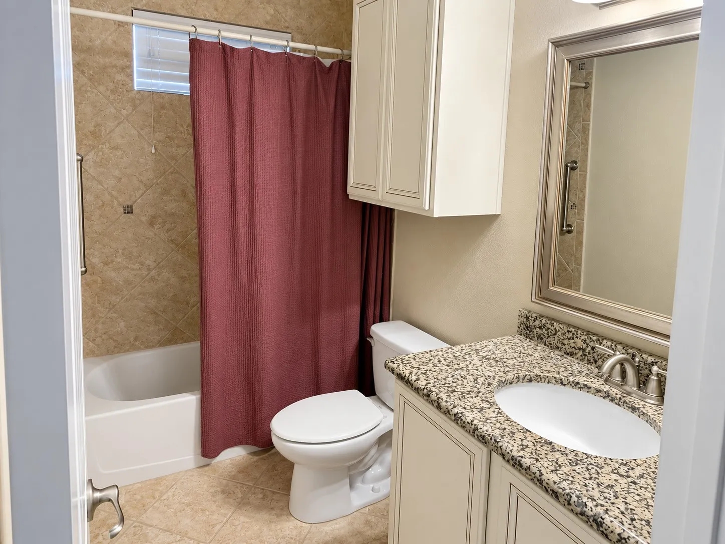 Spa-inspired bathroom featuring dual vanities with speckled stone countertops, a white porcelain vessel sink, framed mirror with integrated lighting, and an updated bathtub-shower combination with tile surround and burgundy curtain enclosure