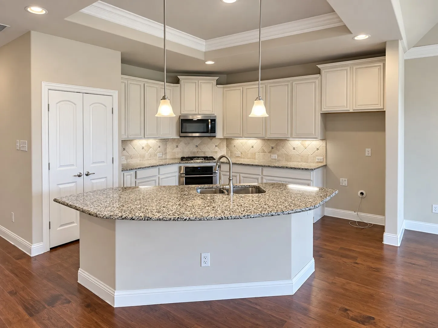 Kitchen featuring a curved central island with a granite countertop, dual pendant lighting, stainless steel double oven, and wood-finish flooring