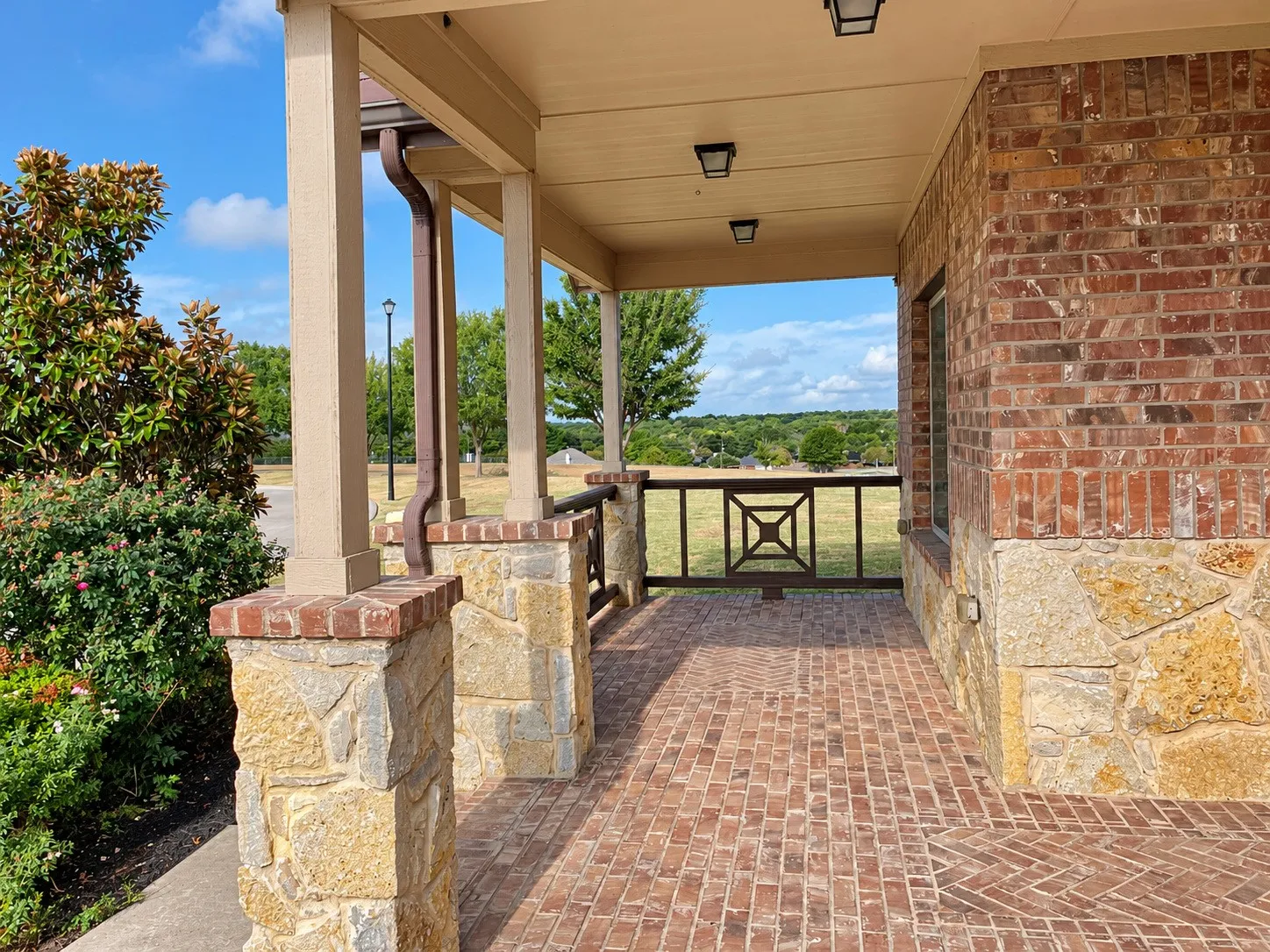 Covered porch featuring brick and stone masonry, decorative metal railing, wood-finish columns, and a brick paver floor