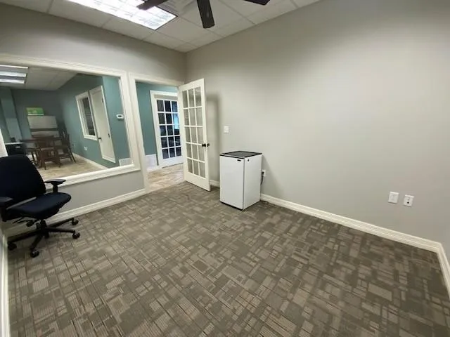 Unfurnished office featuring ceiling fan, french doors, and a drop ceiling
