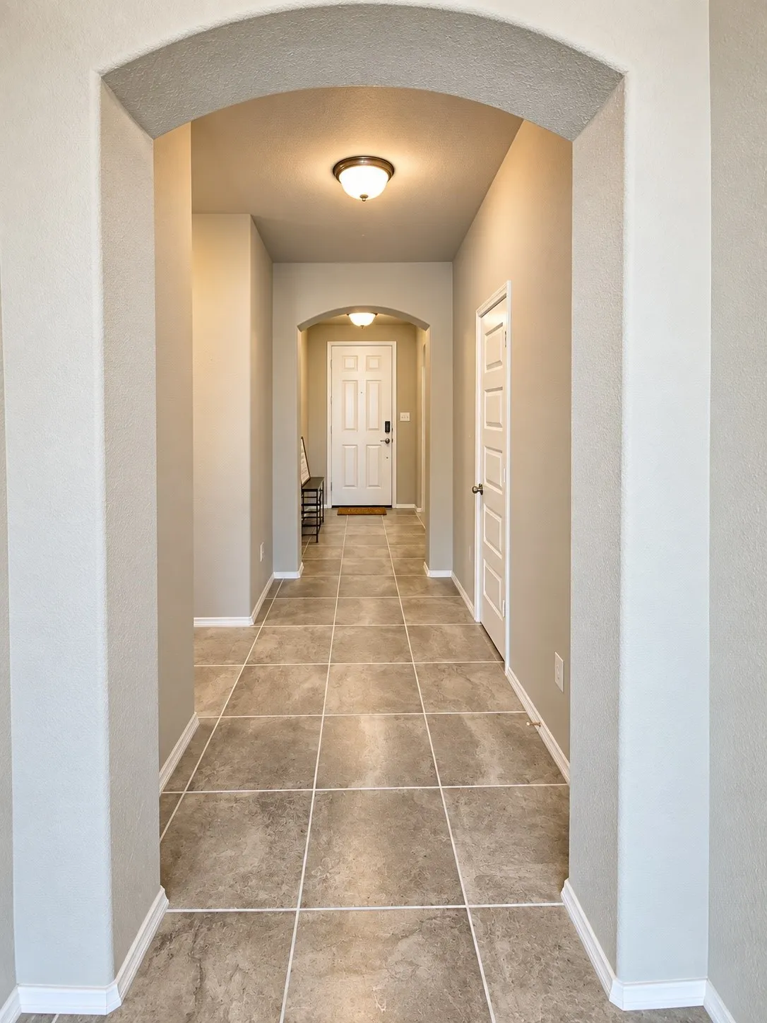 Arched entryway leading to a tiled hallway with recessed lighting and paneled interior doors