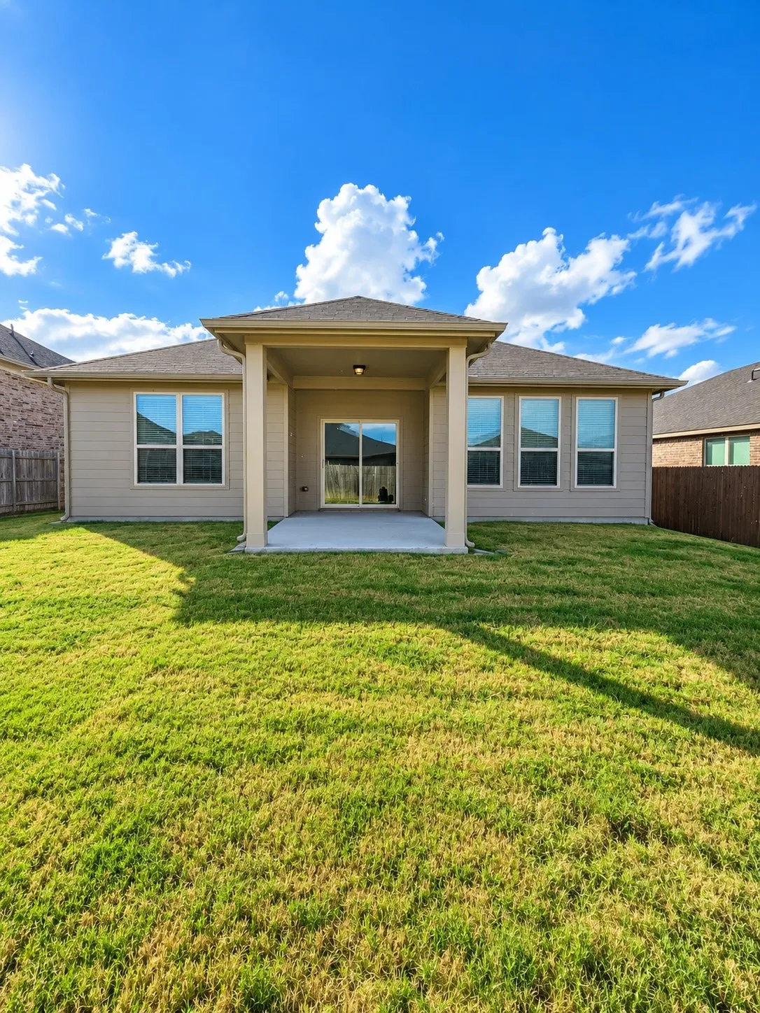 Expansive backyard featuring a covered patio, sliding glass door, multiple large windows, and a privacy fence