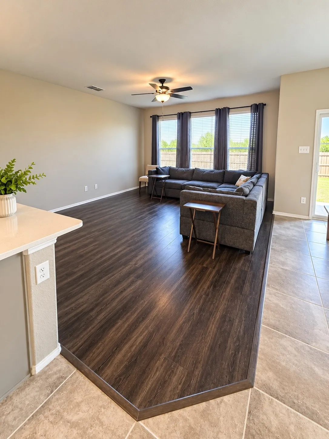 Spacious living area featuring wood-finish flooring, a ceiling fan with integrated lighting, and multiple windows