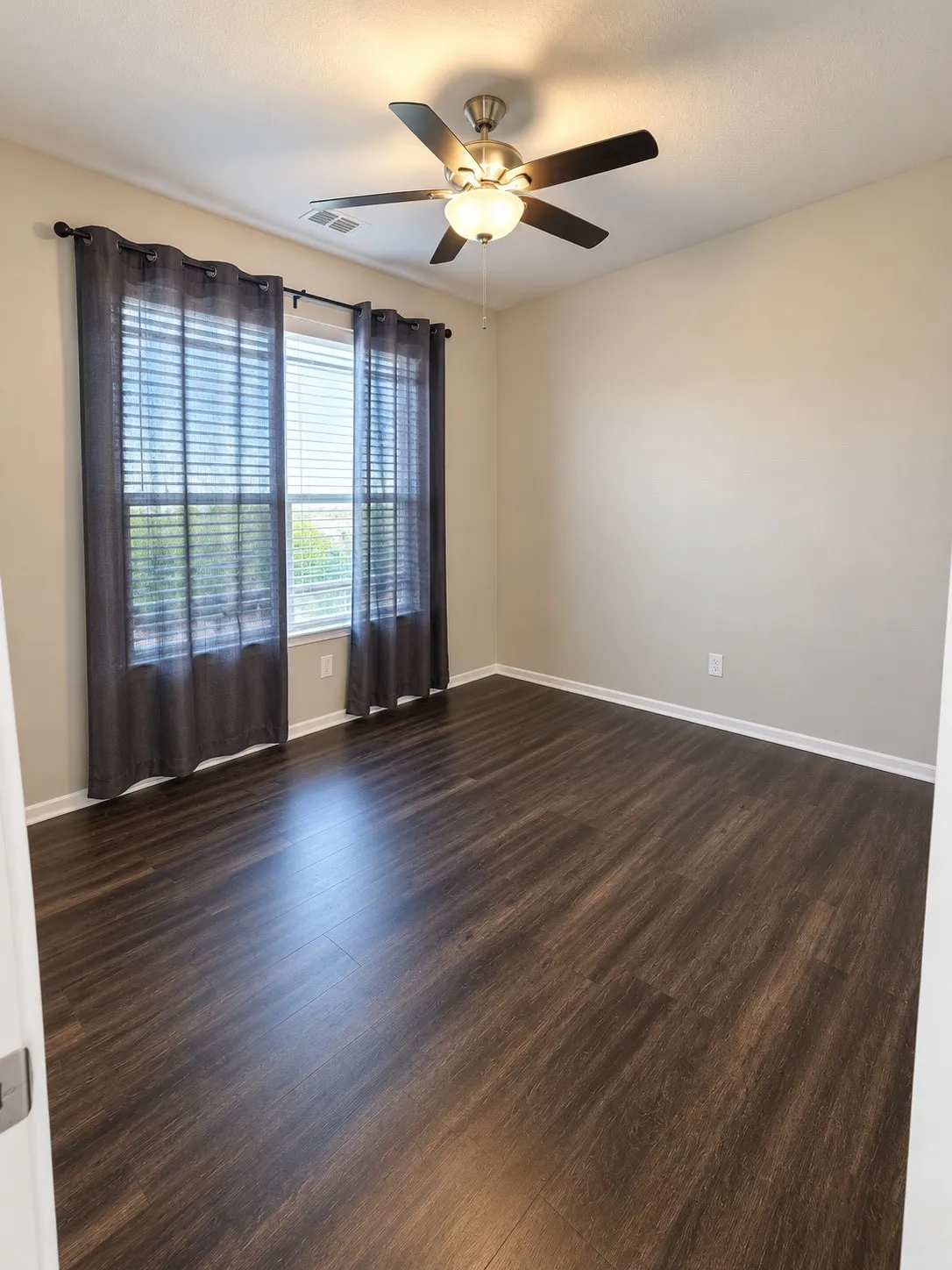 Expansive room featuring wood-finish flooring, a large window with blinds, and a ceiling fan with integrated lighting