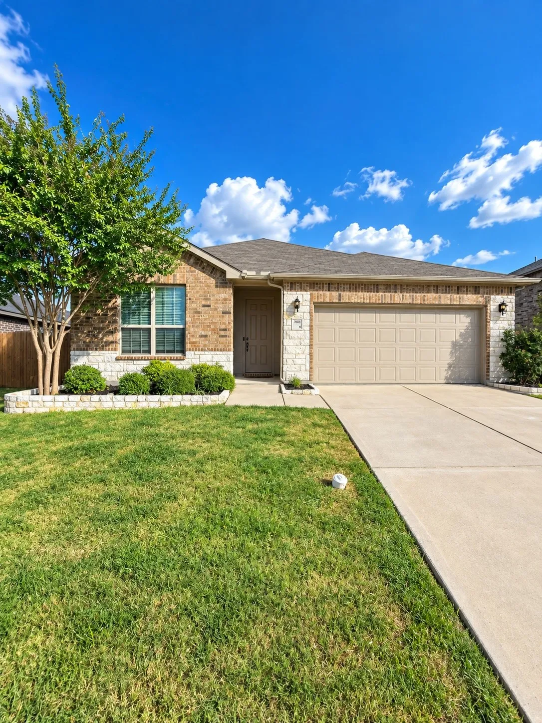 Brick and stone exterior with a neutral garage door, concrete driveway, and front lawn