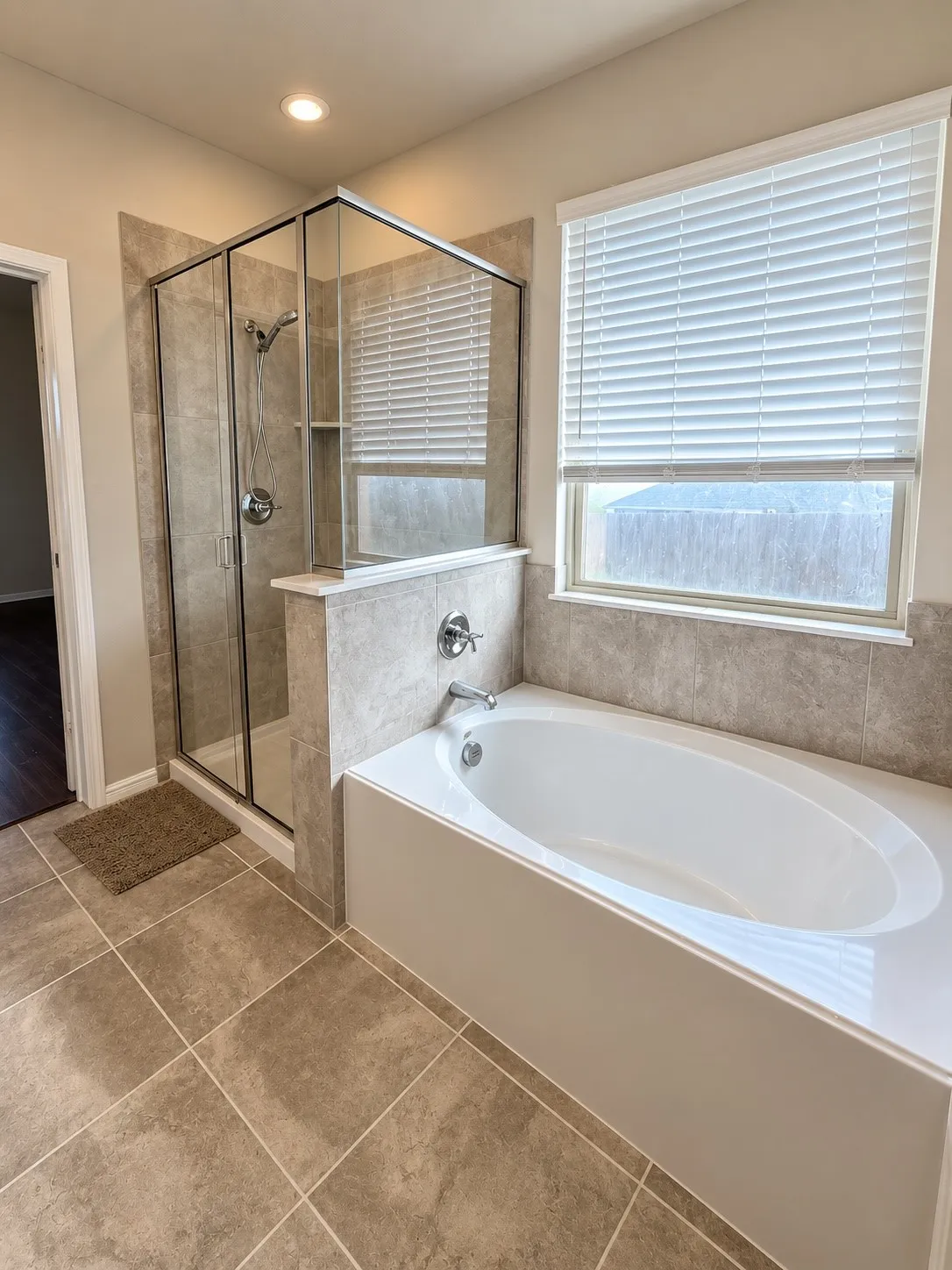 Soaking tub with chrome fixtures, glass-enclosed shower with tile surround, and large format tile flooring