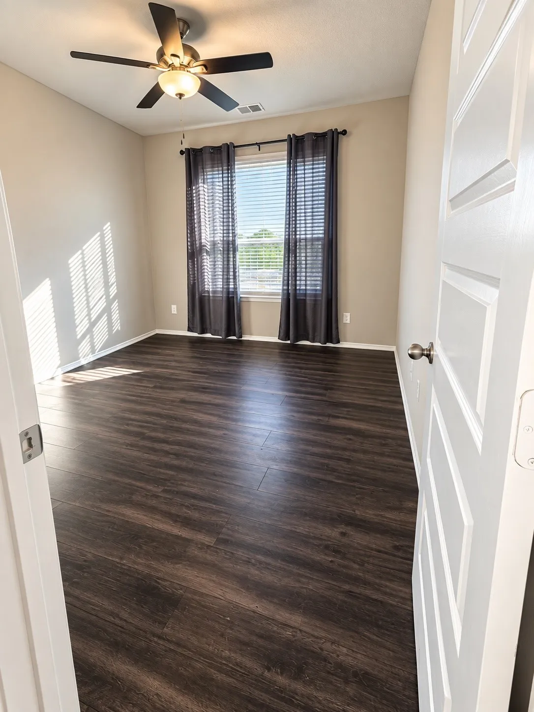 Wood-finish flooring, ceiling fan with integrated lighting, window with blinds, and white panel door
