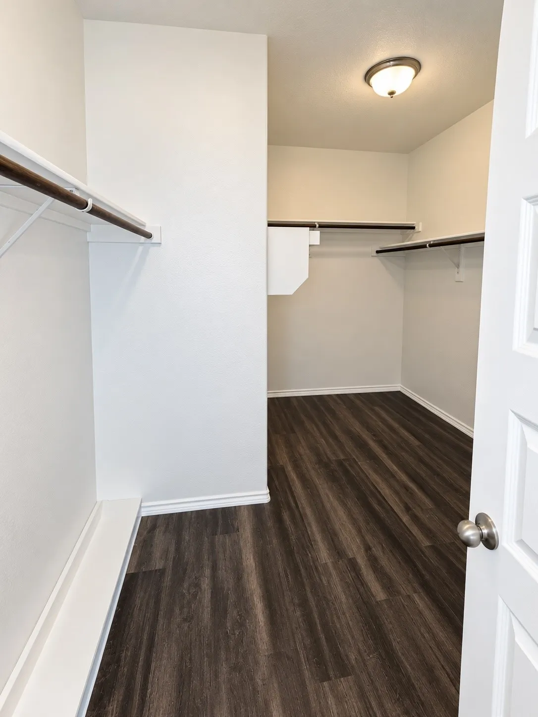 Spacious walk-in closet featuring wood-finish flooring, multiple shelving units, and ample hanging rods