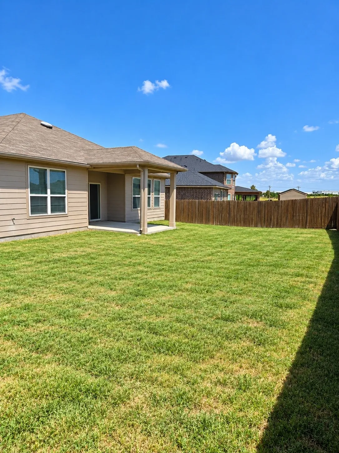 Expansive backyard featuring a covered patio, privacy fencing, and a manicured lawn
