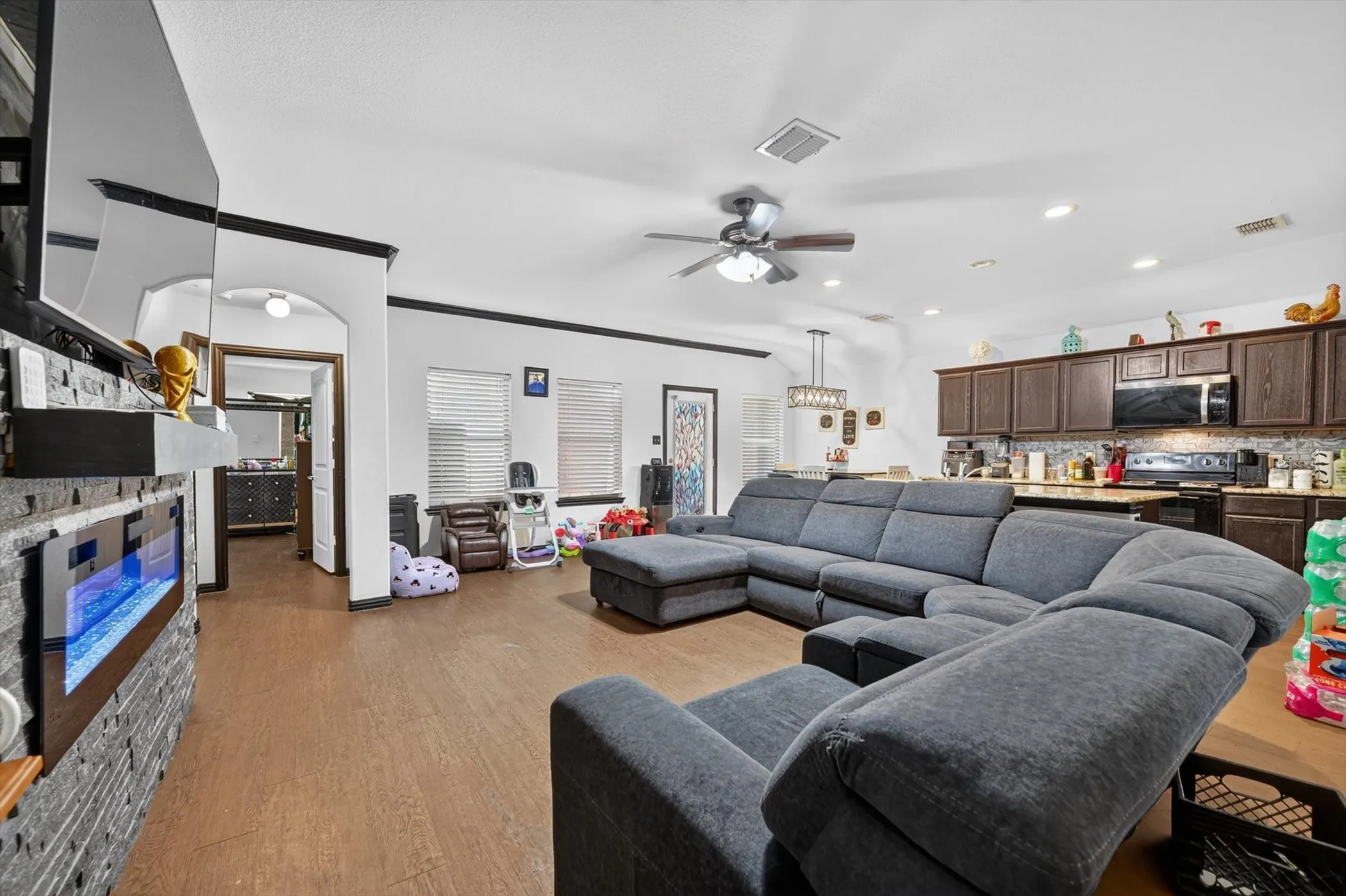 Open-concept floor plan featuring wood-finish flooring, a stone-faced fireplace with an electric insert, recessed lighting, and a ceiling fan