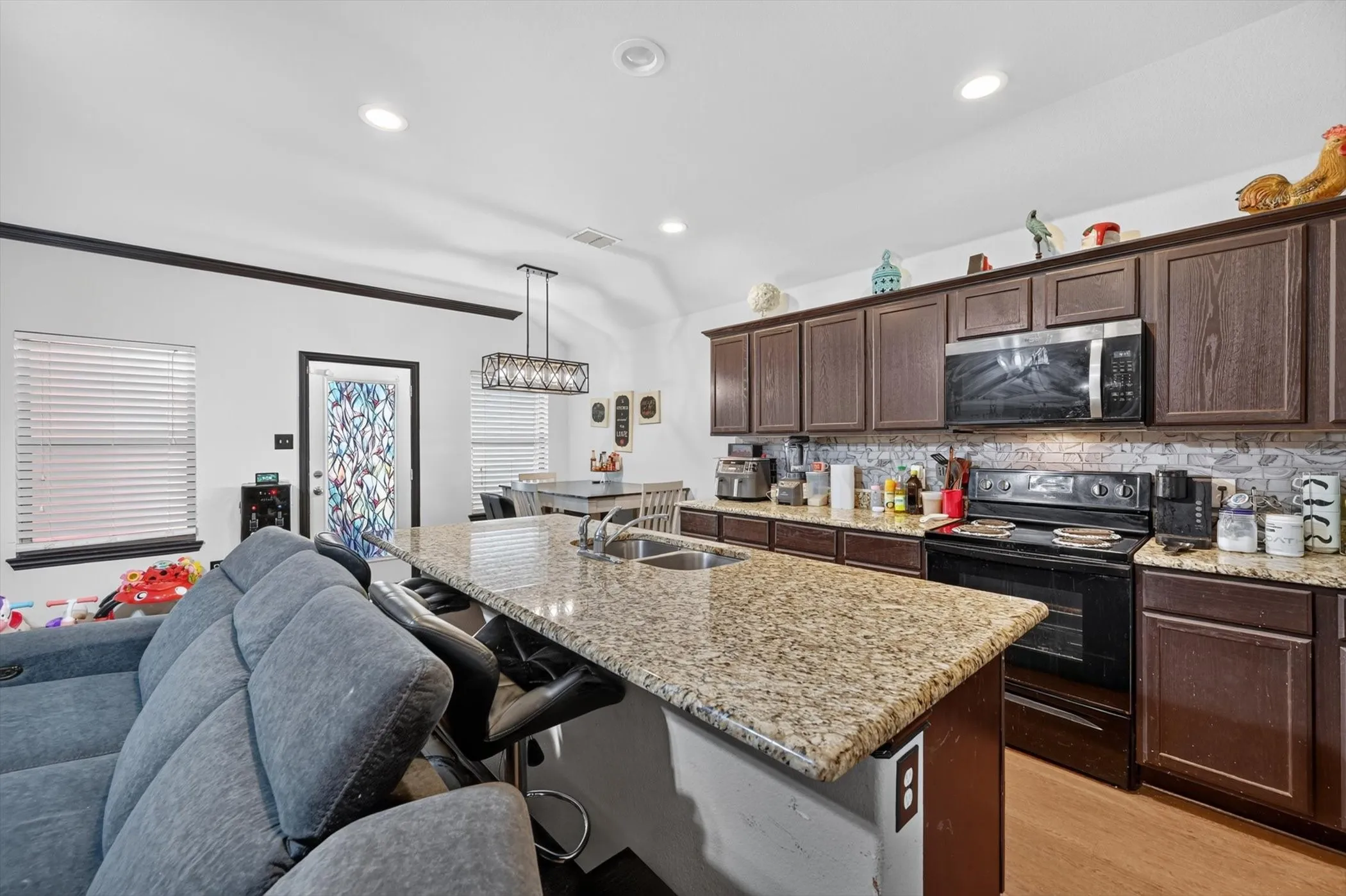 Kitchen featuring a spacious island with an undermount sink, dark wood-finish cabinetry, granite countertops, and a tiled backsplash