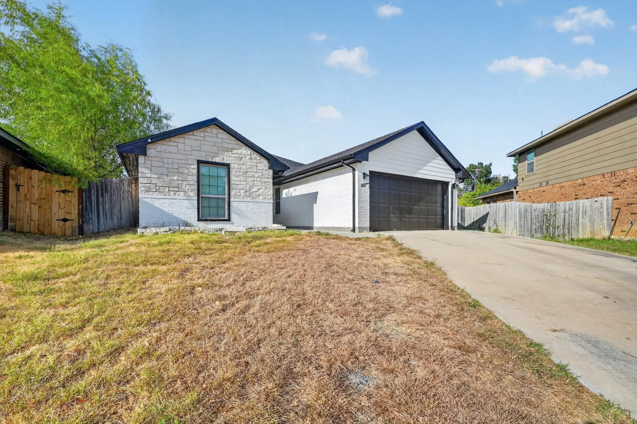 Modern exterior with stone accents, a dark-framed window, an attached garage with a dark garage door, a concrete driveway, and a wooden fence