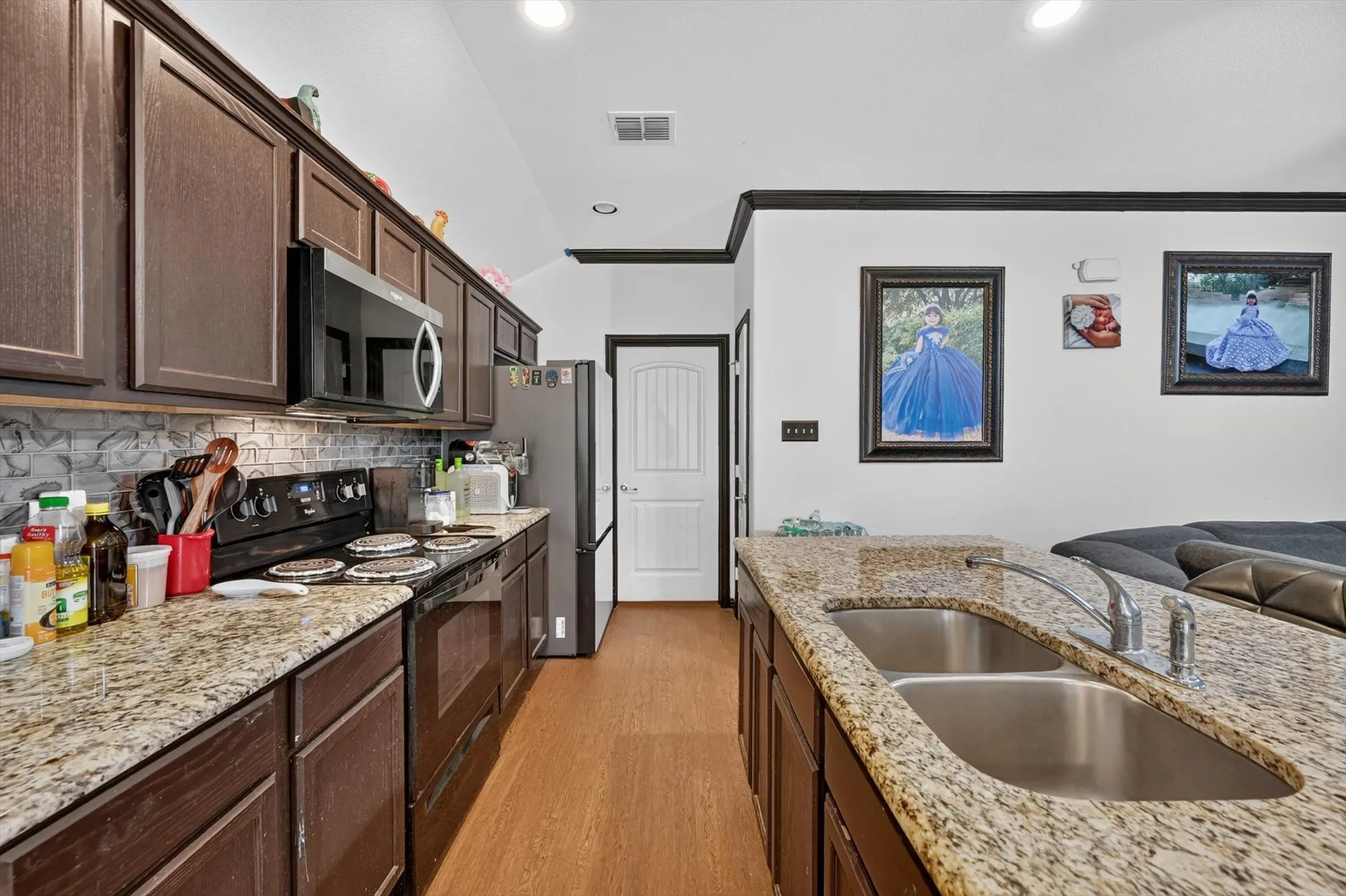 Kitchen featuring wood-finish flooring, dark wood cabinetry, granite countertops, and a tiled backsplash