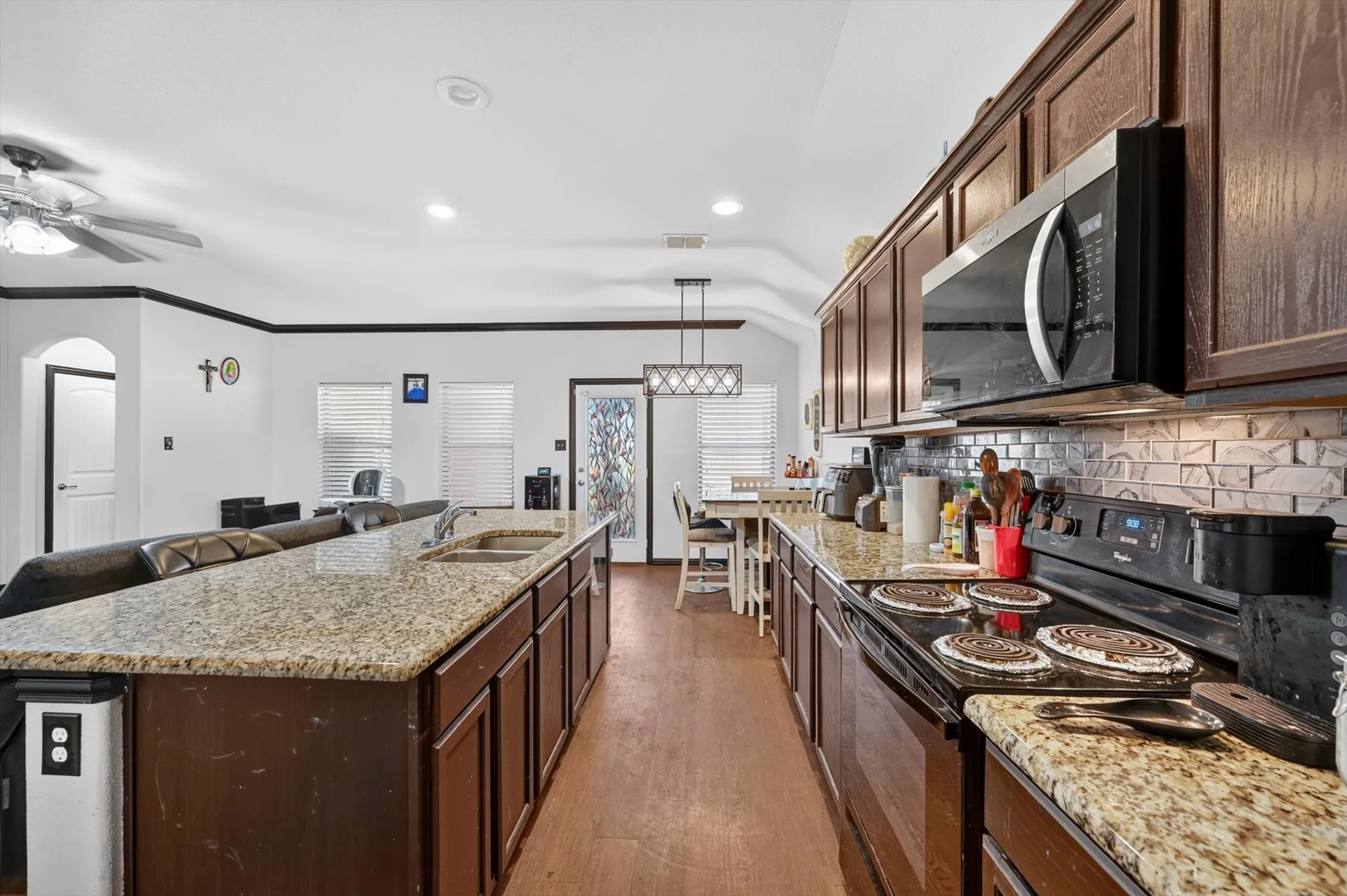 Kitchen featuring granite countertops, wood-finish flooring, dark wood cabinetry, tile backsplash, and an integrated kitchen island