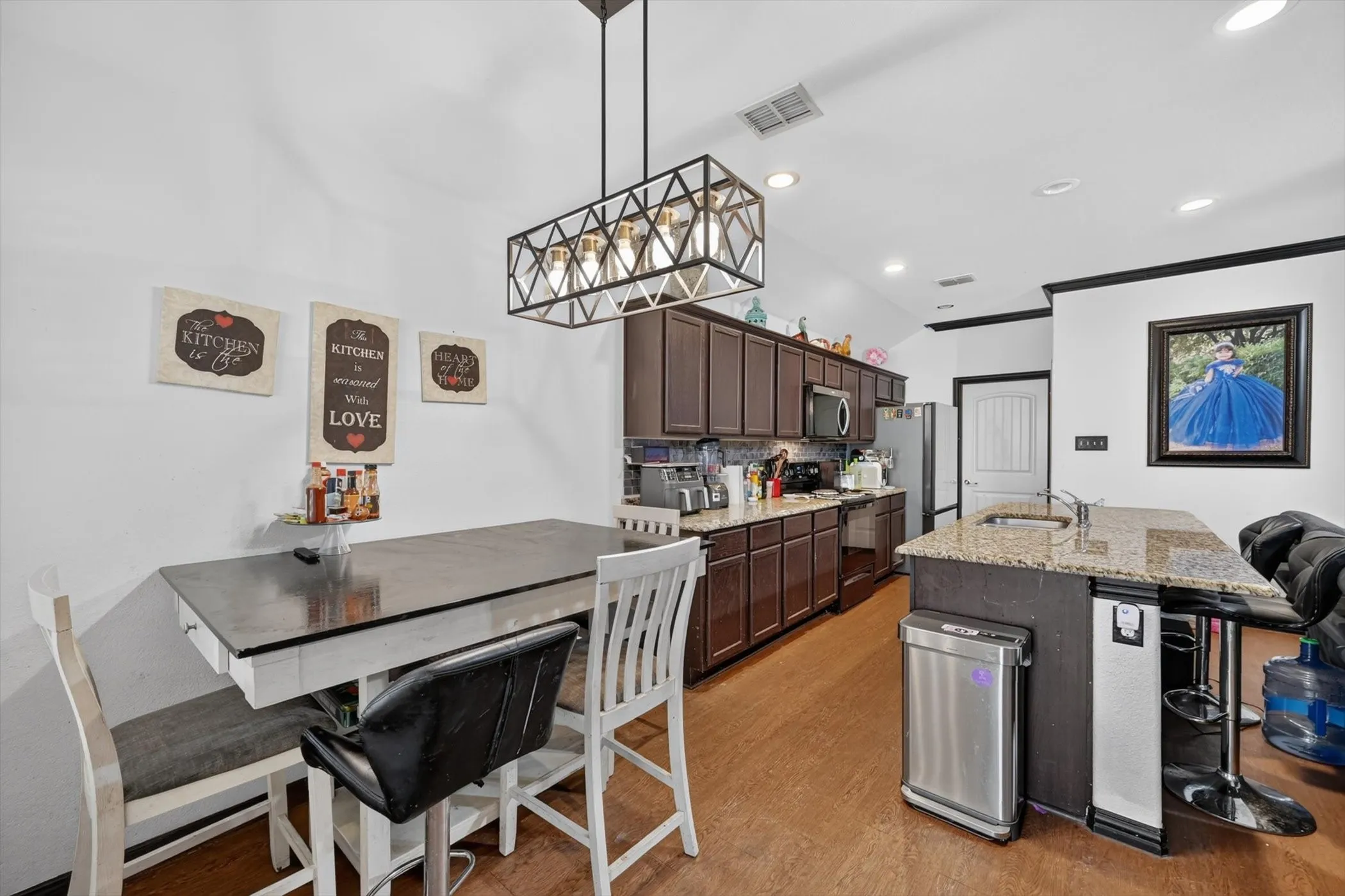 Dark wood-finish cabinetry, stainless steel appliances, speckled stone countertops, wood-finish flooring, and a contemporary linear chandelier