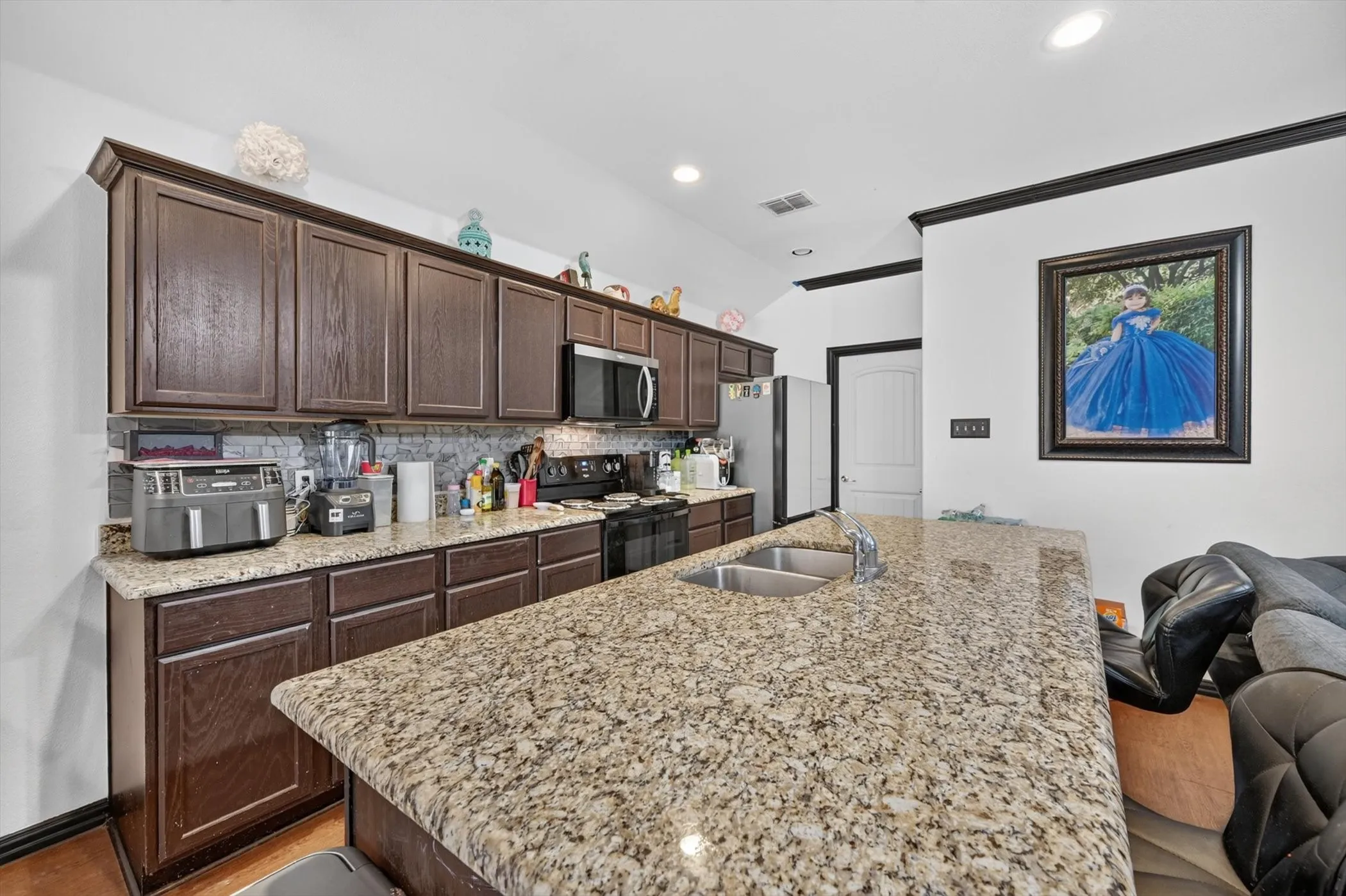 Kitchen featuring a large island with an undermount double basin sink, granite countertops, dark wood-finish cabinetry, and stainless steel appliances