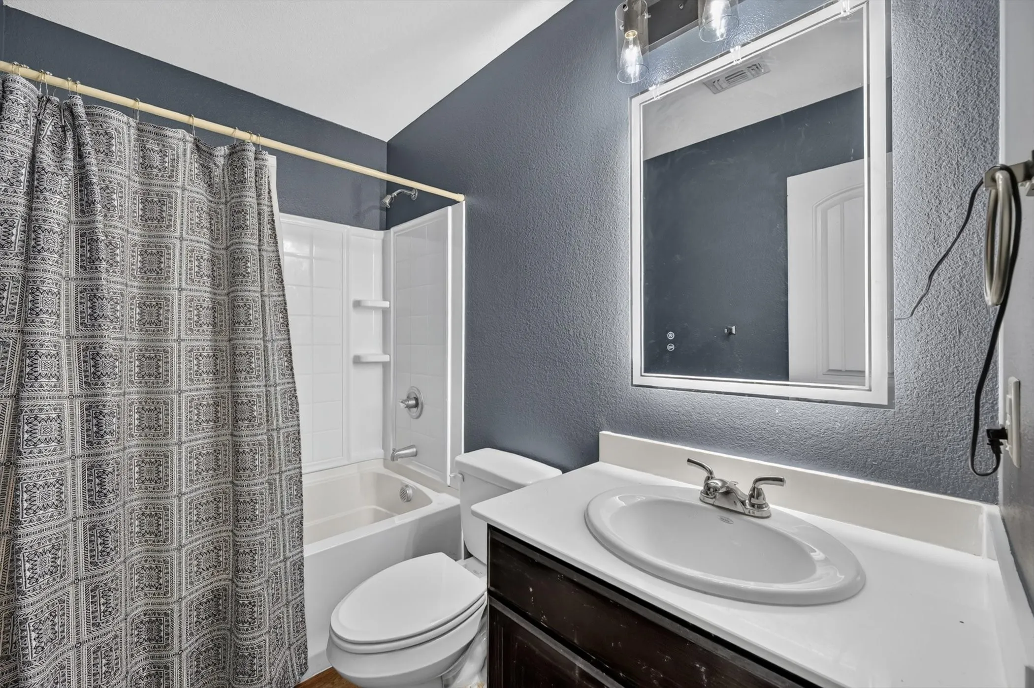 Bathroom featuring a white tub, shower with built-in shelving, dark wood-finish vanity, and a white countertop with an integrated sink