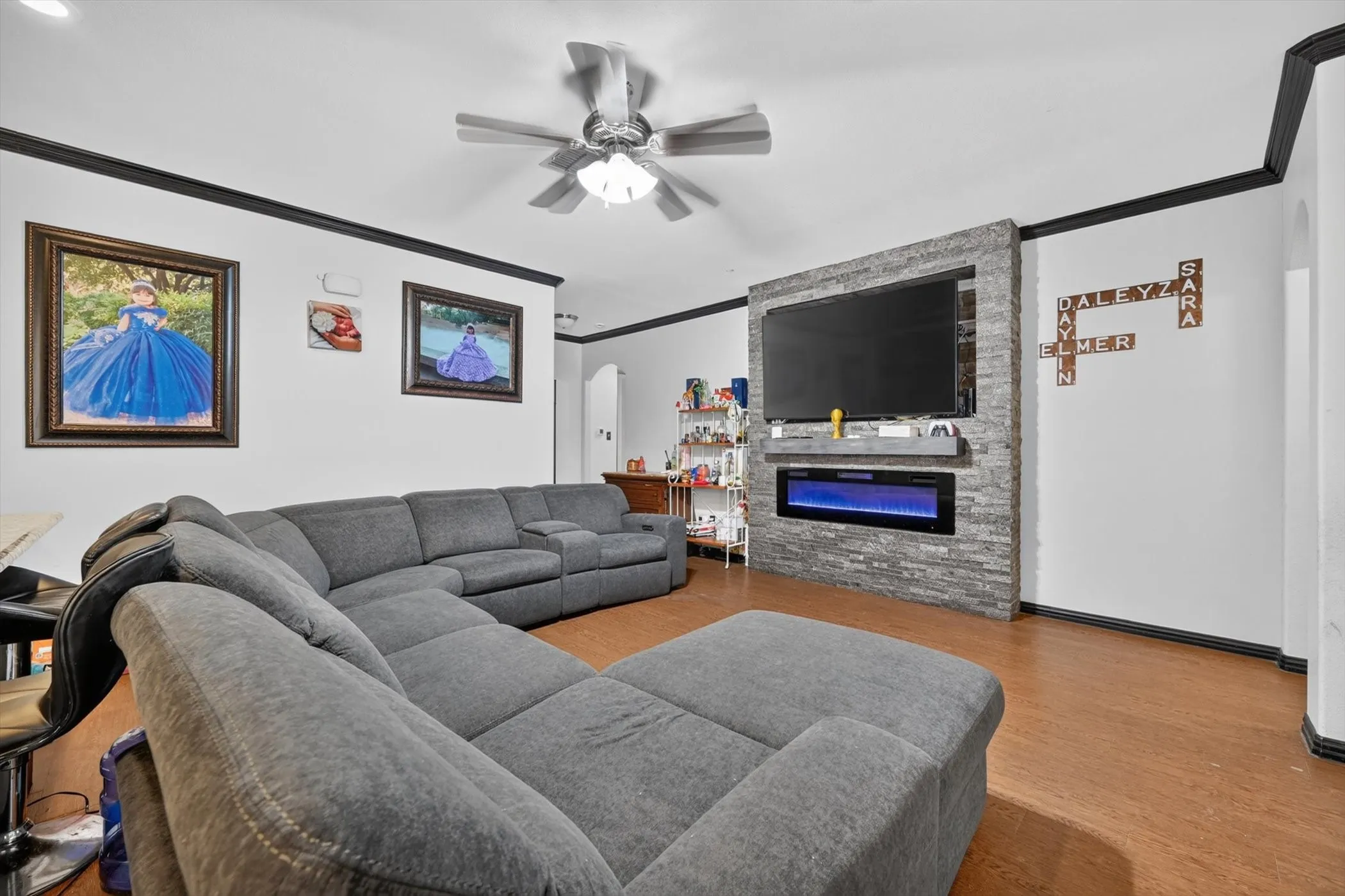 Living area featuring wood-finish flooring, a ceiling fan with integrated lighting, and a stone-clad media wall with a built-in electric fireplace