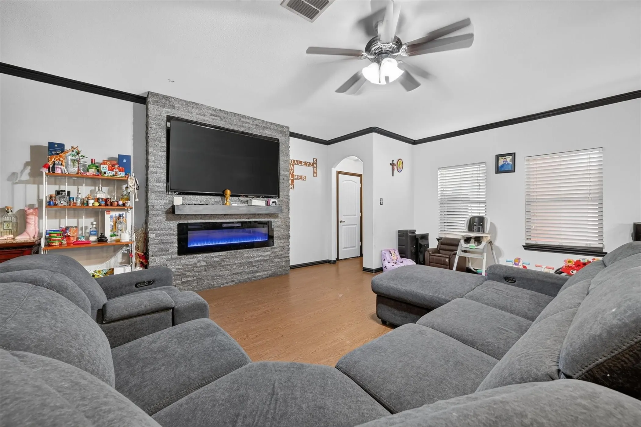 Living area featuring wood-finish flooring, a stacked stone accent wall with an integrated electric fireplace, and a ceiling fan