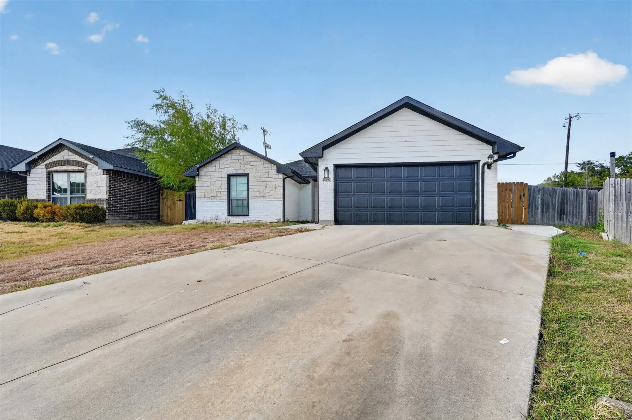 Attached two-car garage with dark paneled door, concrete driveway, and partial wood fencing