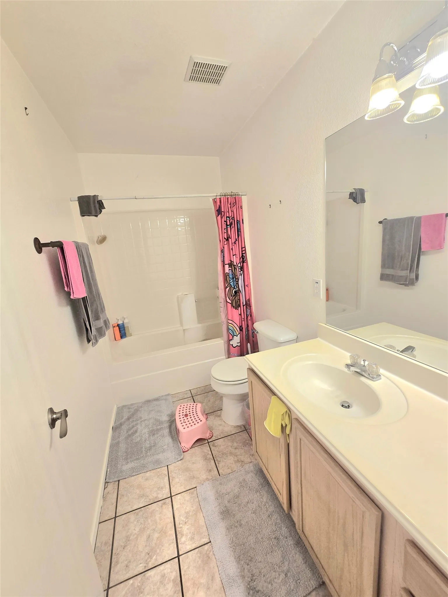 White bathtub with integrated shower, vanity with wood-finish cabinetry, single basin sink, and tile flooring