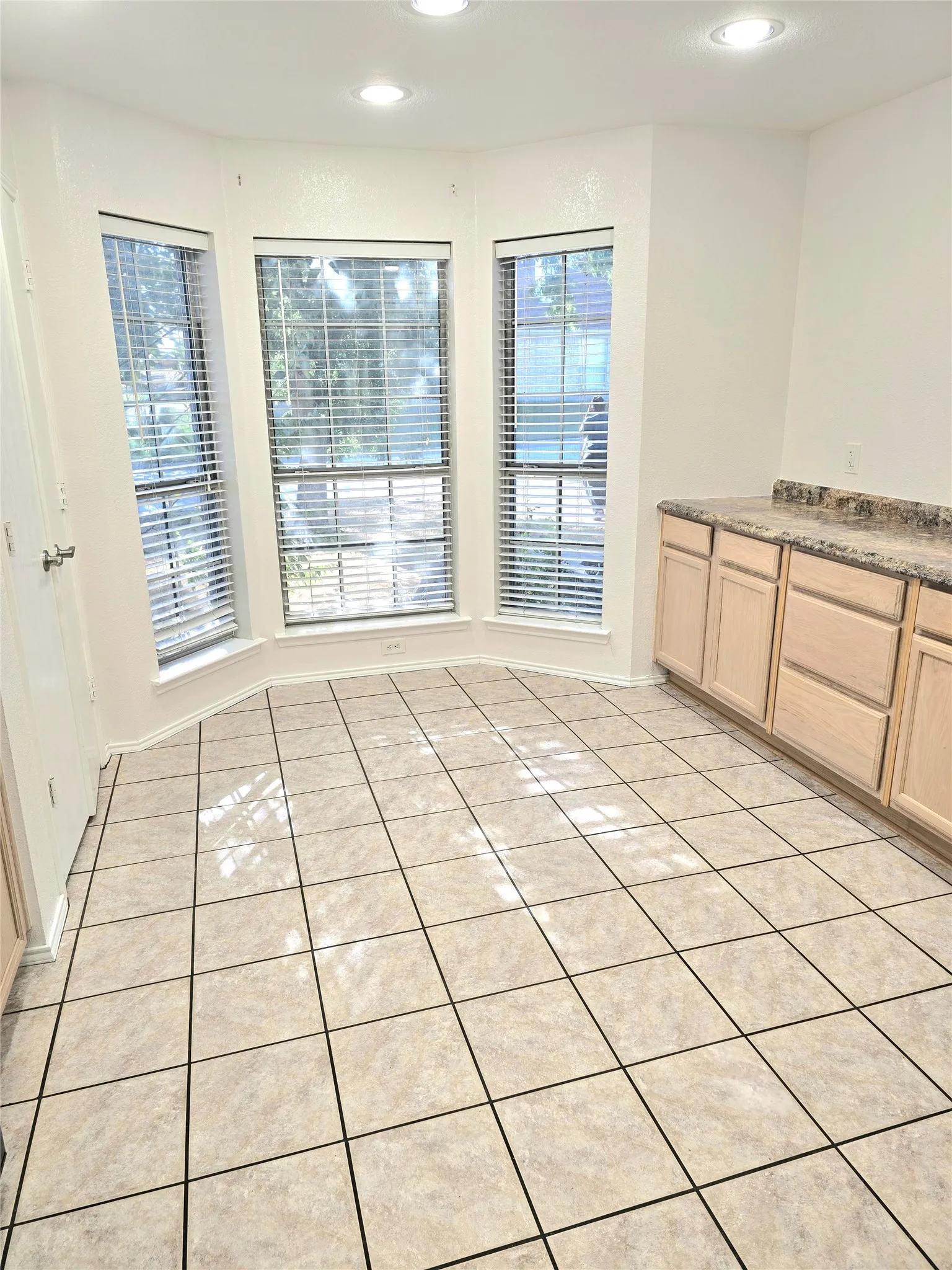 Bay window with multiple windows, recessed ceiling lighting, tile flooring, and a built-in cabinet with a stone-finish countertop