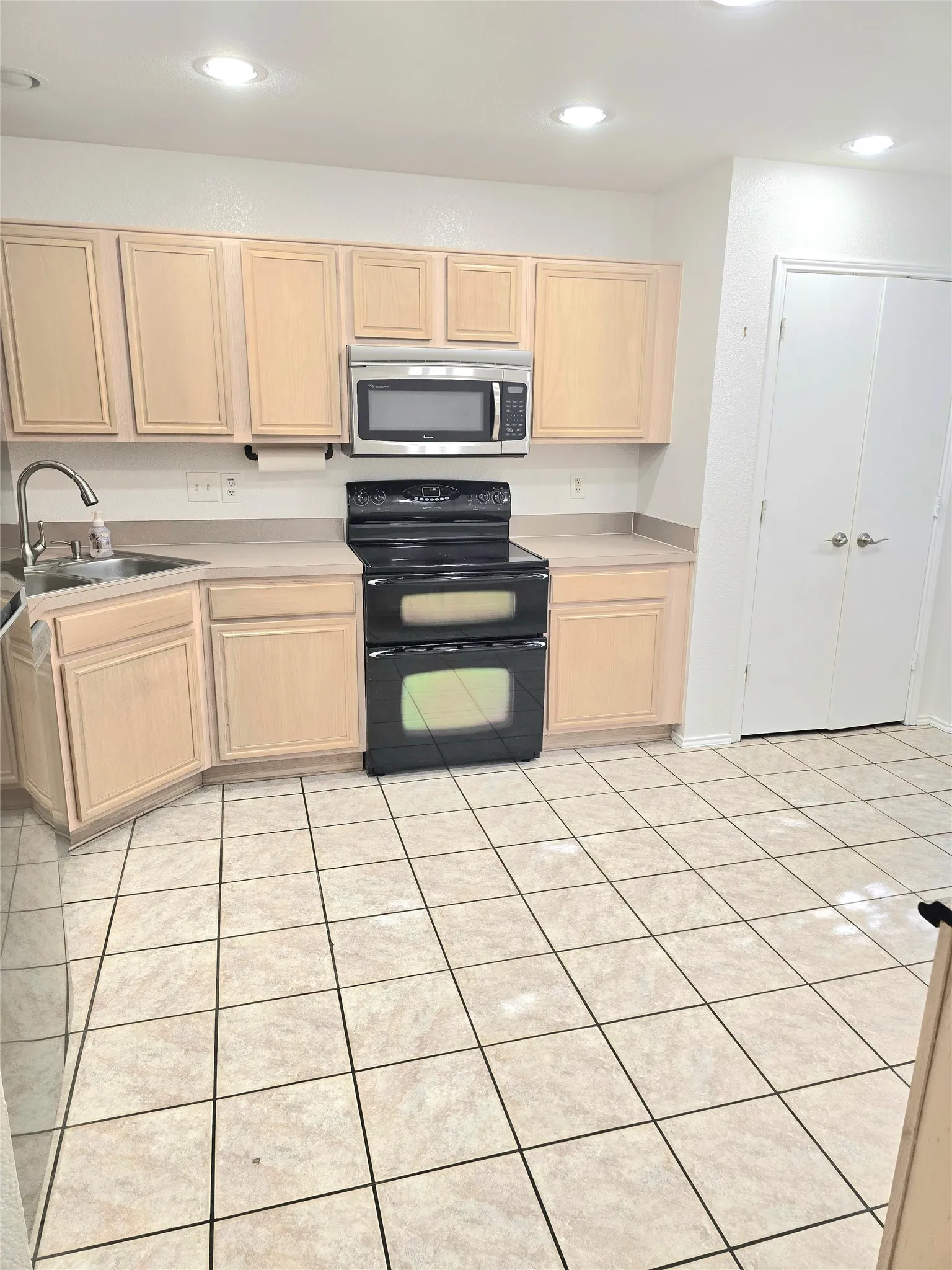 Recessed ceiling lighting, light wood-finish cabinetry, stainless steel microwave, black electric range, and light tile flooring