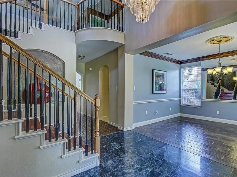 Two-story foyer featuring a wood-finish staircase with wrought iron balusters, a grand chandelier, and mixed tile flooring