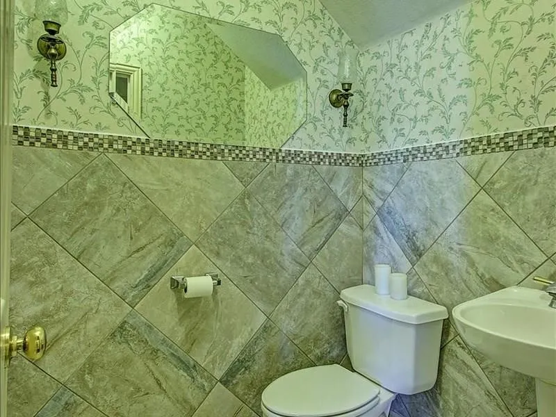 Diagonal floor-to-ceiling wall tiling, decorative mosaic tile border, patterned wallpaper, octagonal wall mirror, and dual wall sconces