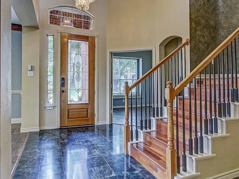 Two-story foyer featuring dark tile flooring, a wood staircase with black iron spindles, and a wood entry door with leaded glass