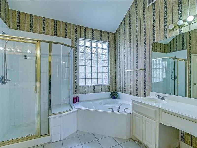 Bathroom featuring a glass-enclosed shower, corner soaking tub, glass block window, and dual vanity with integrated sink